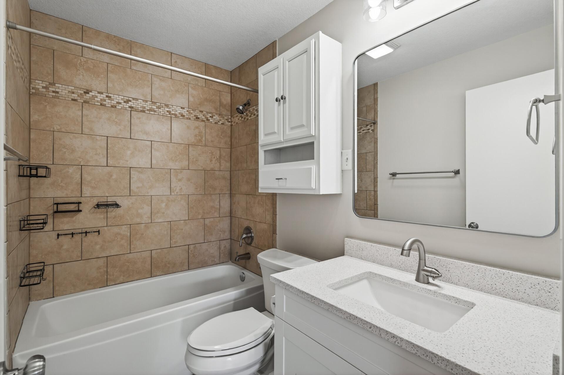 The main level bathroom is conveniently located near both bedrooms and the main living areas, making it ideal for guests and everyday use. It features a crisp white vanity, modern mirror, updated hardware, and a clean, tiled tub/shower.