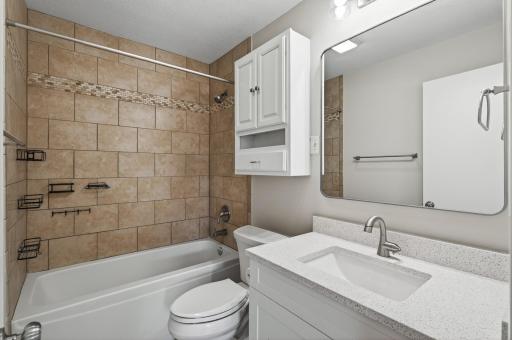 The main level bathroom is conveniently located near both bedrooms and the main living areas, making it ideal for guests and everyday use. It features a crisp white vanity, modern mirror, updated hardware, and a clean, tiled tub/shower.