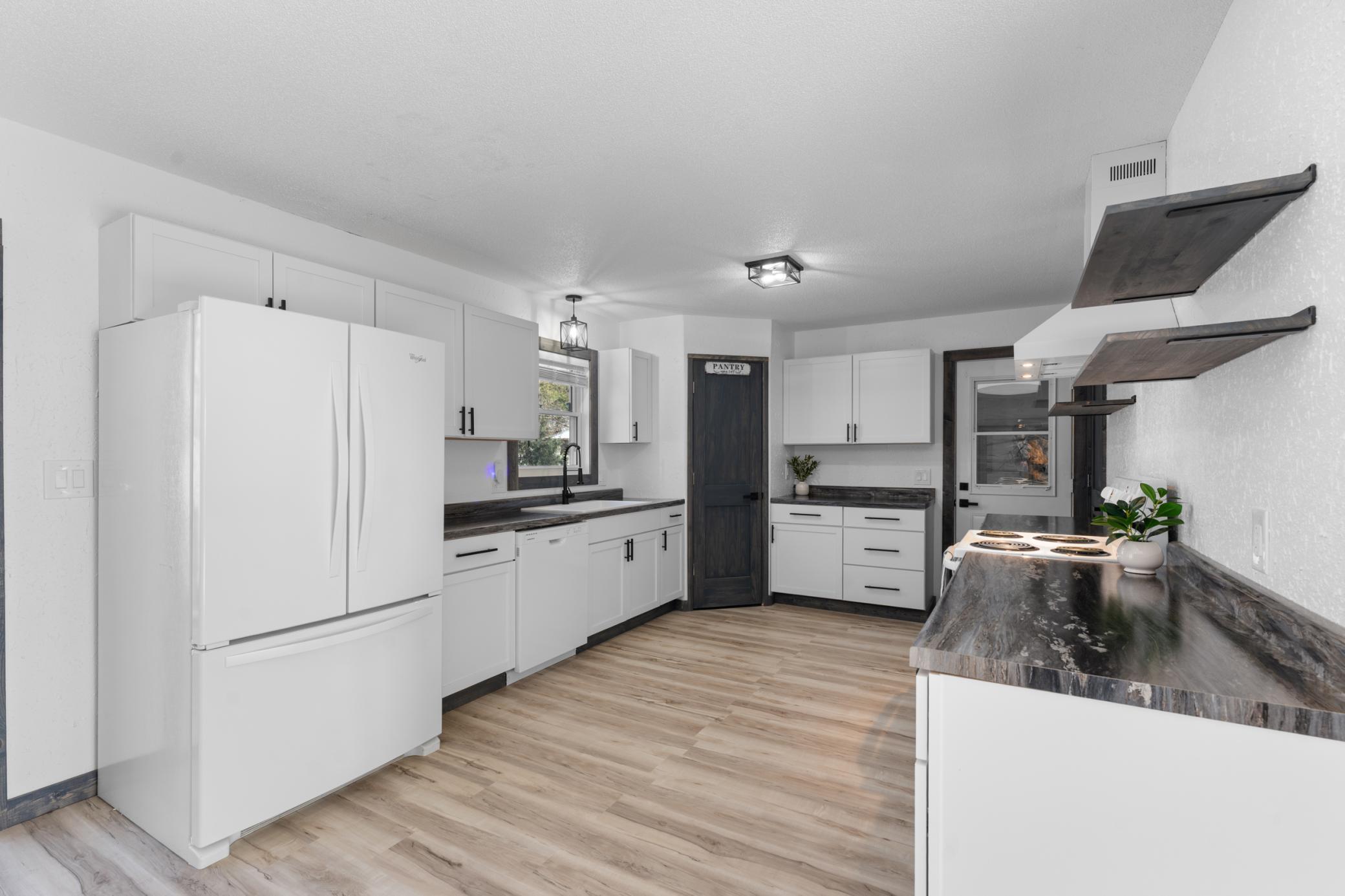 The kitchen offers crisp white cabinetry, sleek hardware and lighting, a pantry for extra storage, and a convenient kitchen window.