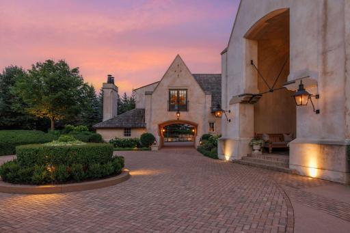 Winding paver driveway, flanked by lush landscaping, and elegant gas lanterns.