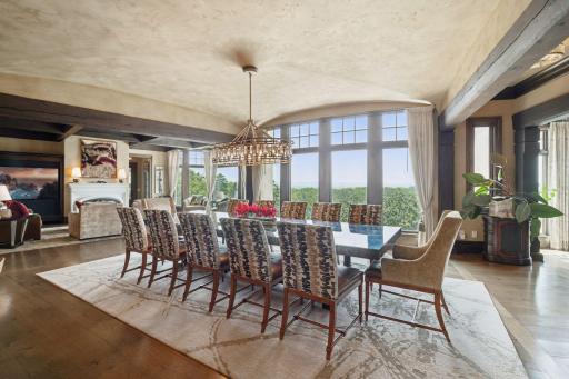 The dining room is a grand spectacle, featuring massive windows that showcase panoramic views of the breathtaking landscape beyond. Sunlight pours in, illuminating the space and enhancing the warm tones.