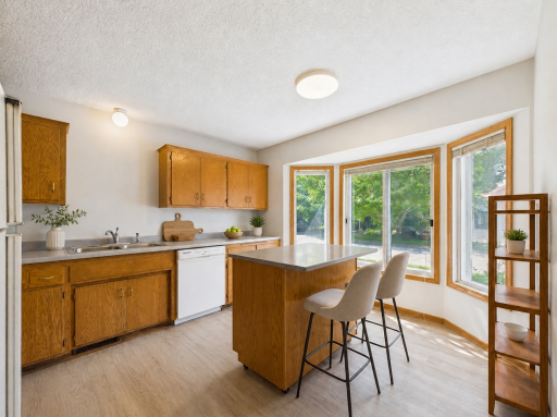 Apple Valley, MN townhome kitchen with bay window, virtually staged to show potential island and counter seating. Existing cabinetry, countertops, flooring, windows, and appliances are shown as photographed.