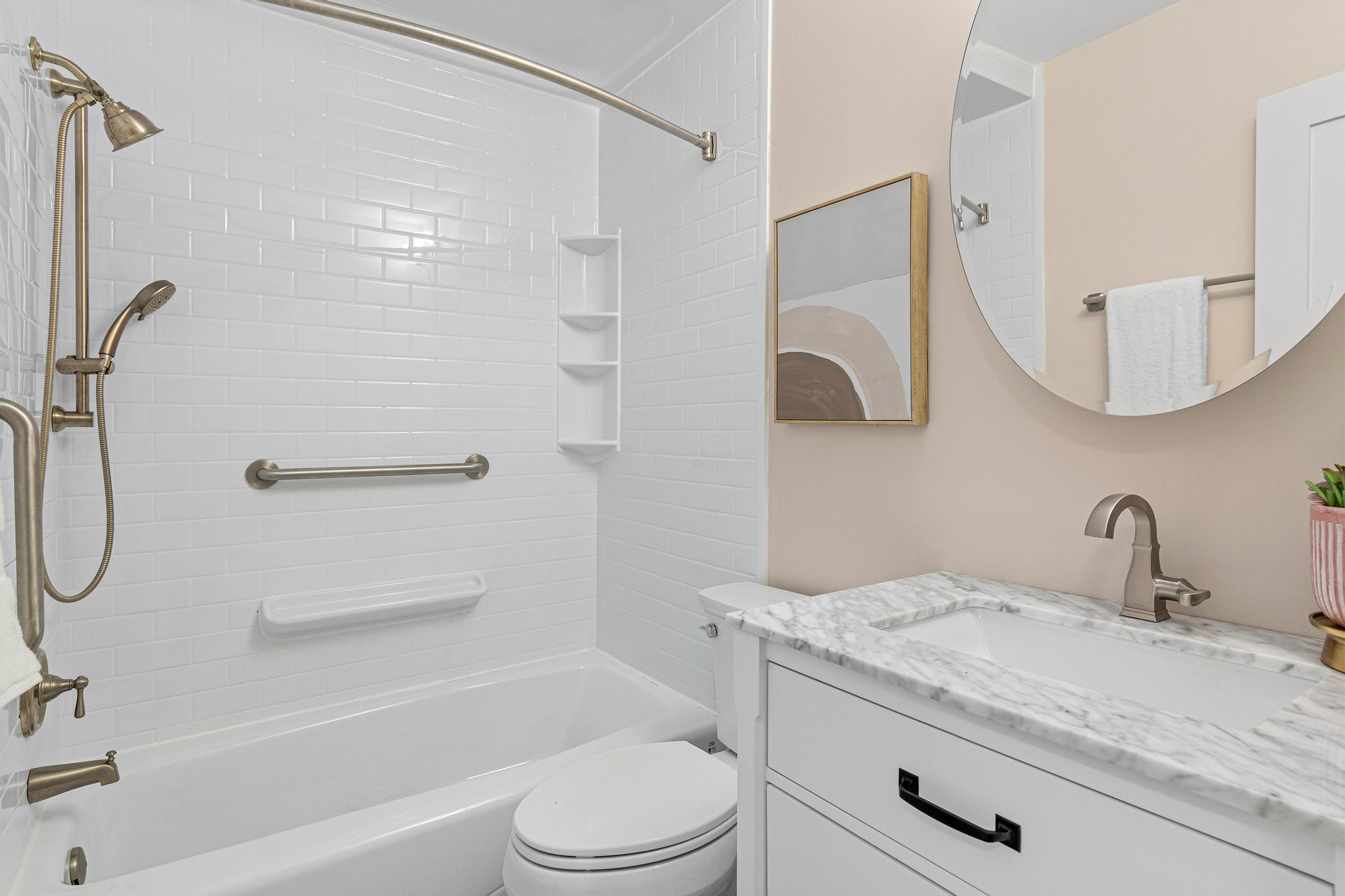 Lower level full bathroom with updated vanity, countertop, light fixtures, tub surround, toilet, heated floor and plumbing fixtures.