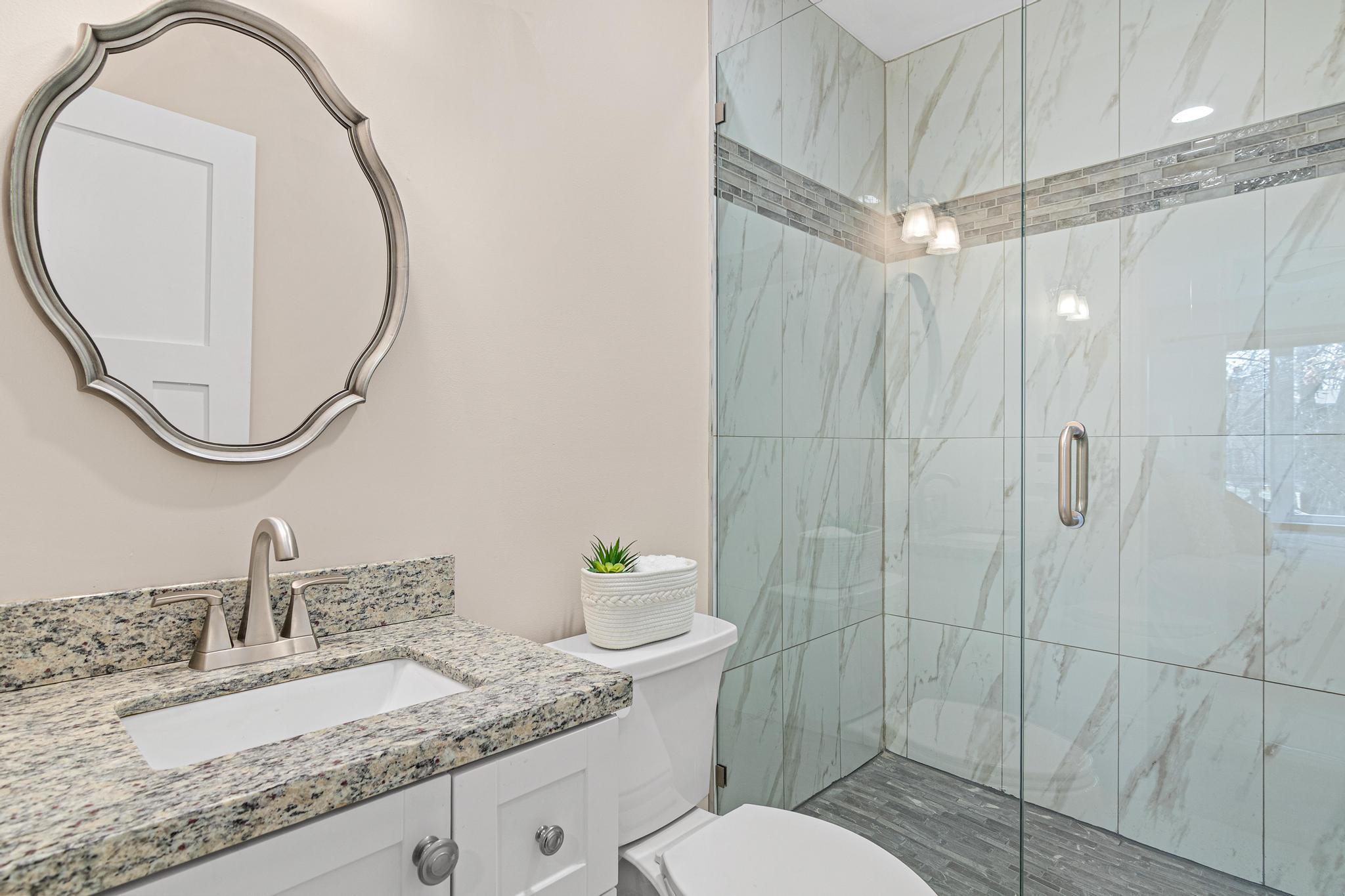 Primary bedroom 3/4 bathroom with updated vanity, light fixture, toilet and a gorgeous tiled walk-in shower and glass surround!