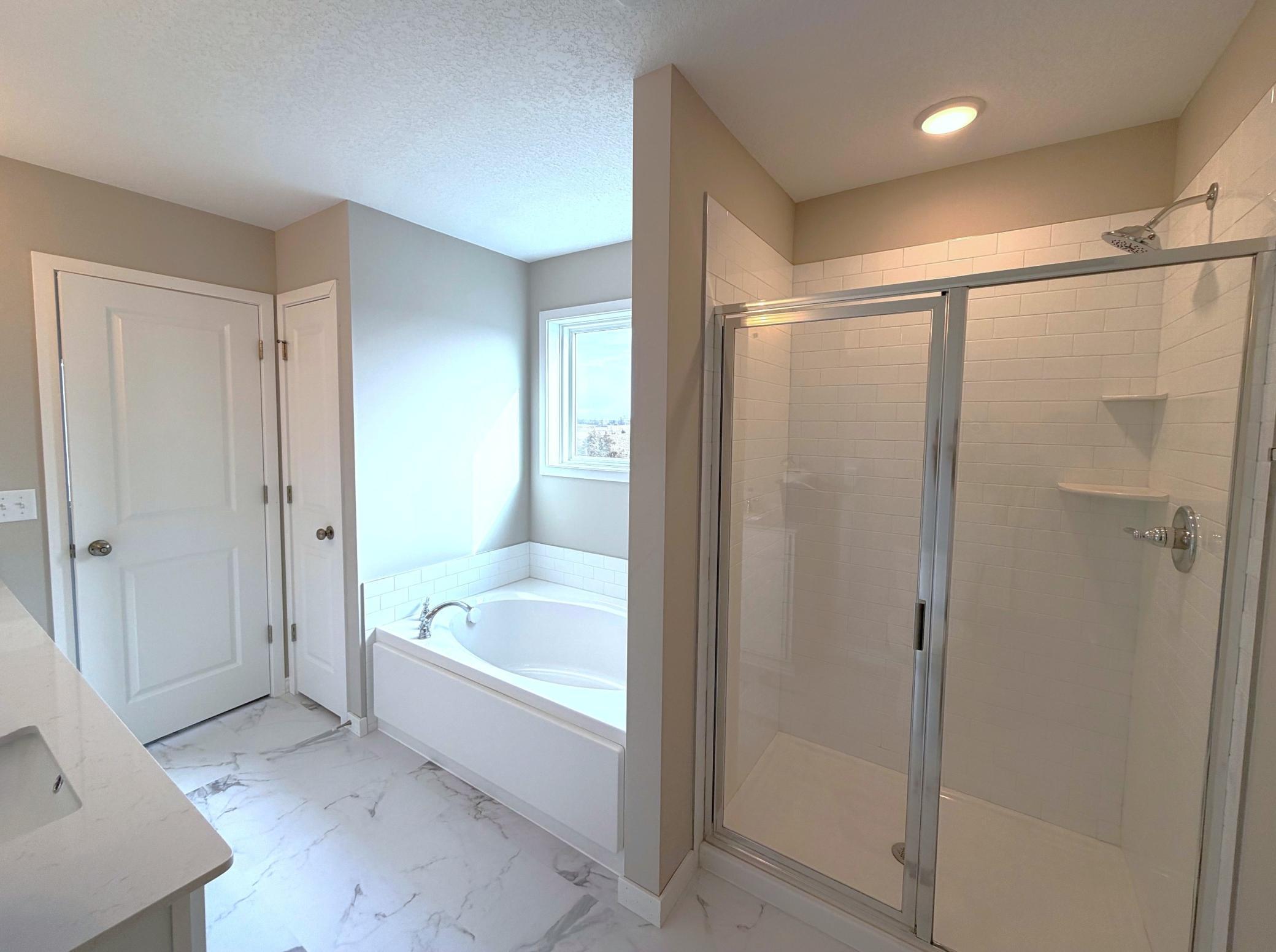 PHOTO OF A DIFFERENT HOME WITH SIMILAR PLAN. FINISHES MAY VARY. Primary Suite Deluxe Bath features a Soaking Tub, Shower with Tile Wall Surround, Shower Door, and Linen Closet.
