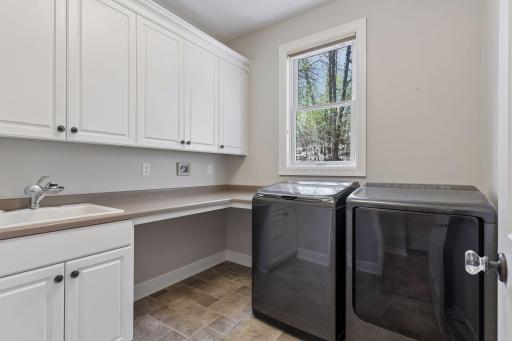 Main level laundry room with upper & lower built-ins, folding countertop & utility sink