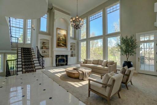 A showstopping living room with soaring ceilings and custom built-ins centers around a statement fireplace, complemented by an impressive open staircase with a balcony overlook that anchors the space. (virtually staged)