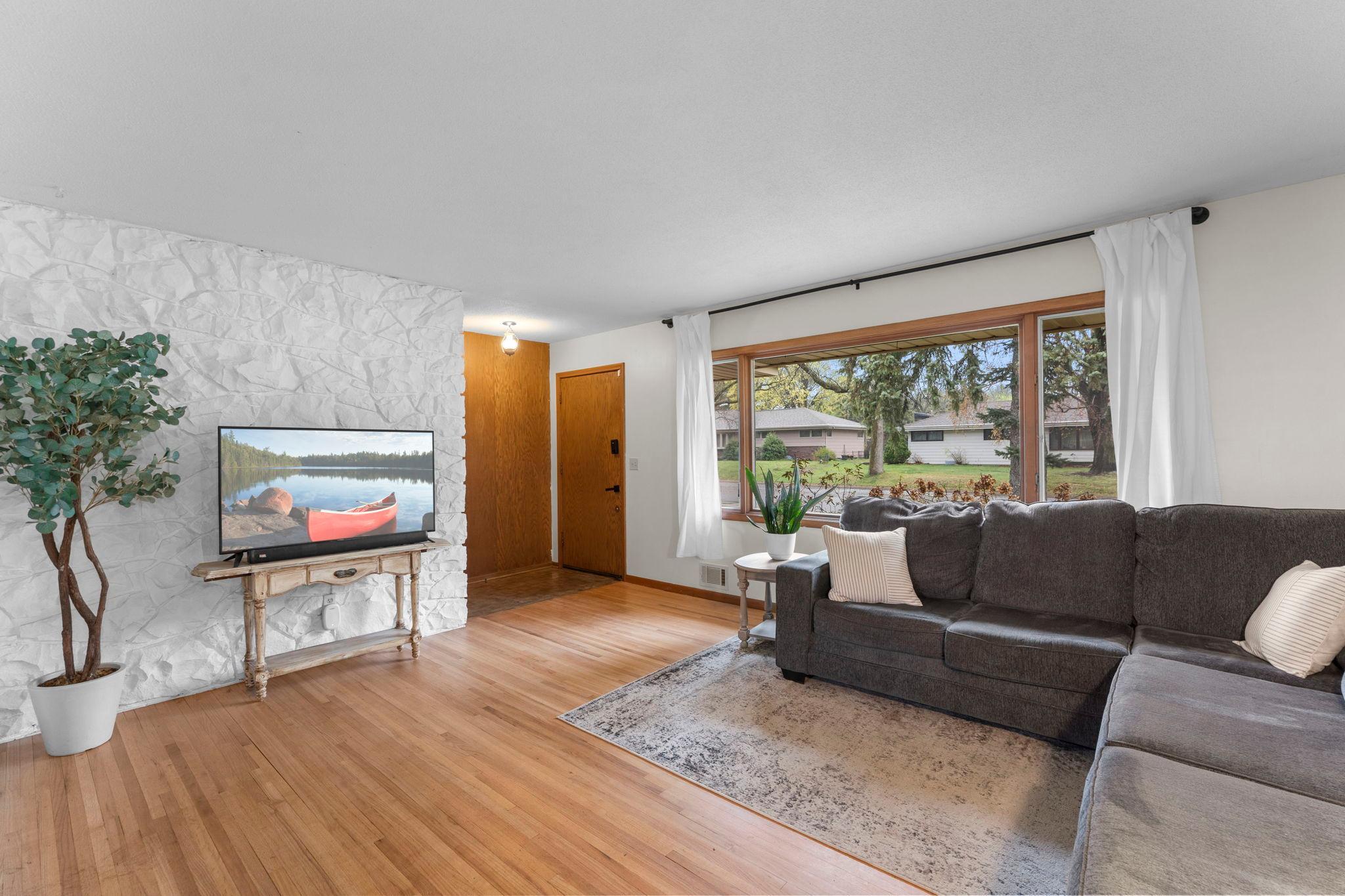 The light-filled living room welcomes you with timeless wood flooring, expansive front-facing windows, and a striking stone accent wall sourced from the Iron Range, creating a true focal point full of character.
