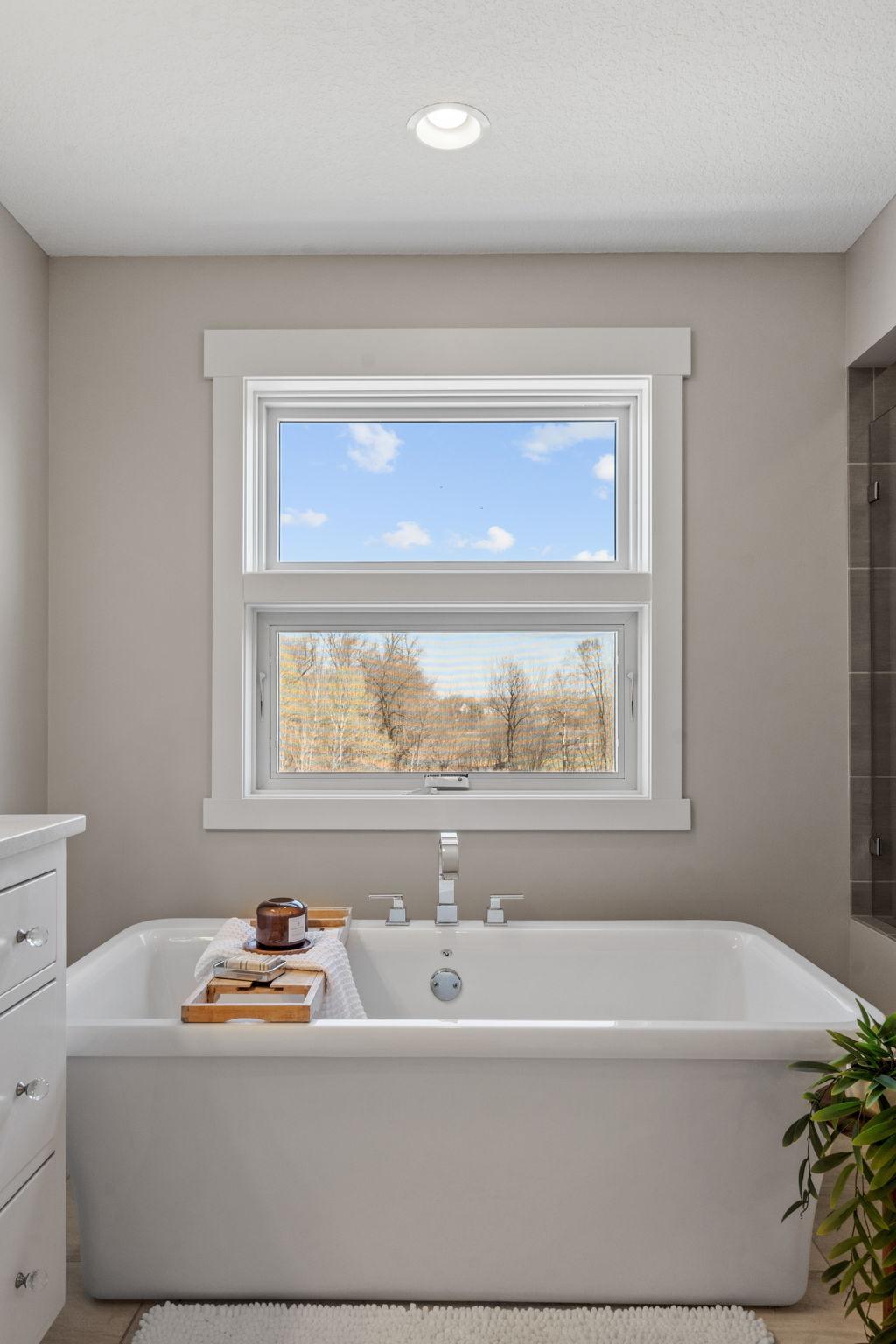 Soaking tub perfectly positioned beneath the window, creating a peaceful, spa-like retreat with natural light and views.