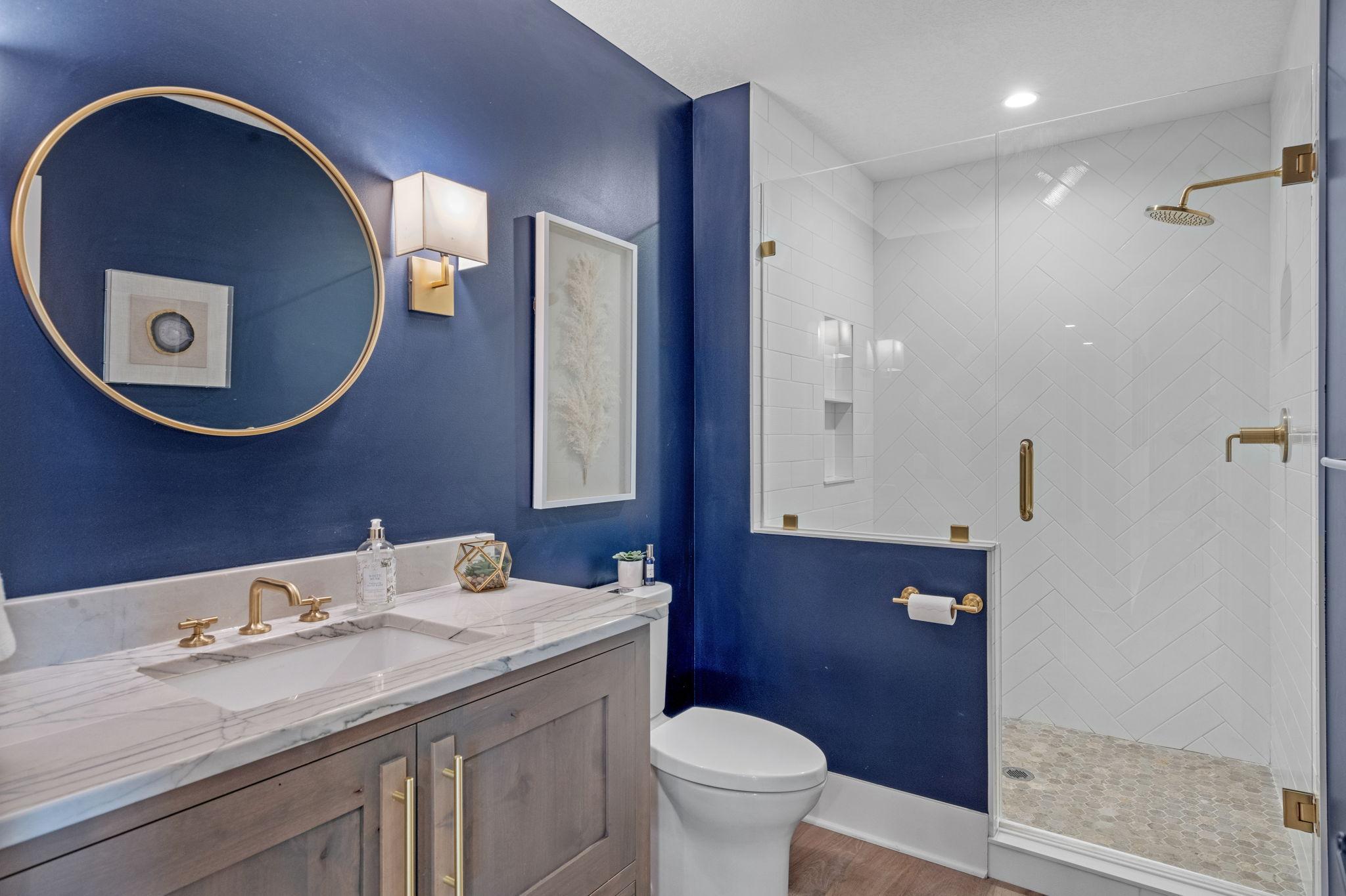 Dark, moody, and done right. This lower level bath brings bold design with rich navy walls, warm brass finishes, and a clean, modern feel.