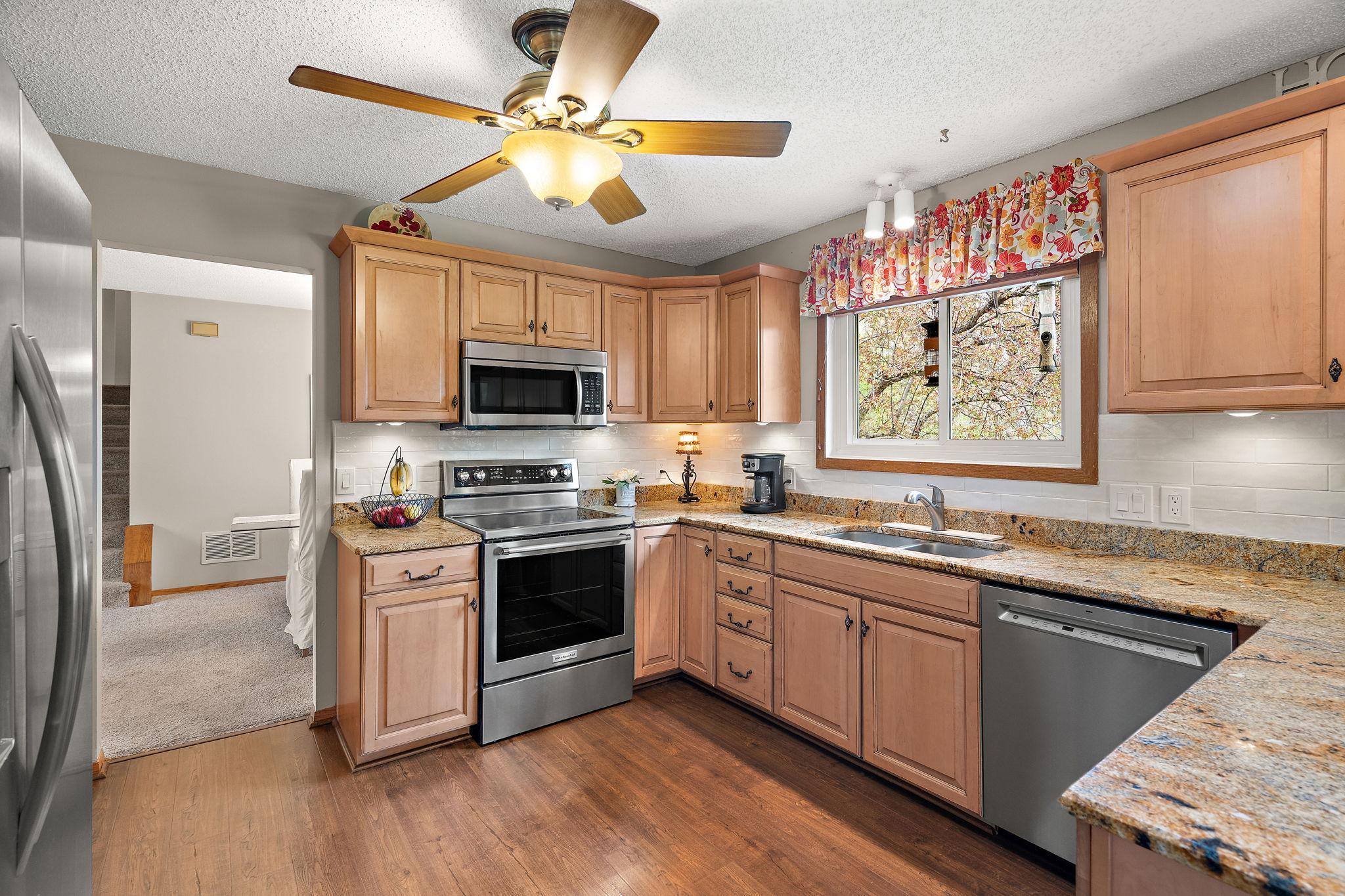 The kitchen features a hardwood floor a view of the backyard from the window over the sink and newer appliances with a microwave replaced in 2024 and refrigerator, stove and dishwasher replaced in 2025.