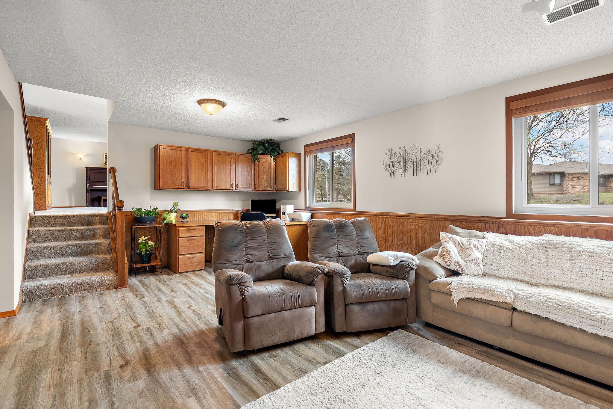A view from the lower level gas fireplace of the recreation room with office area and stairs leading to the main level beyond.