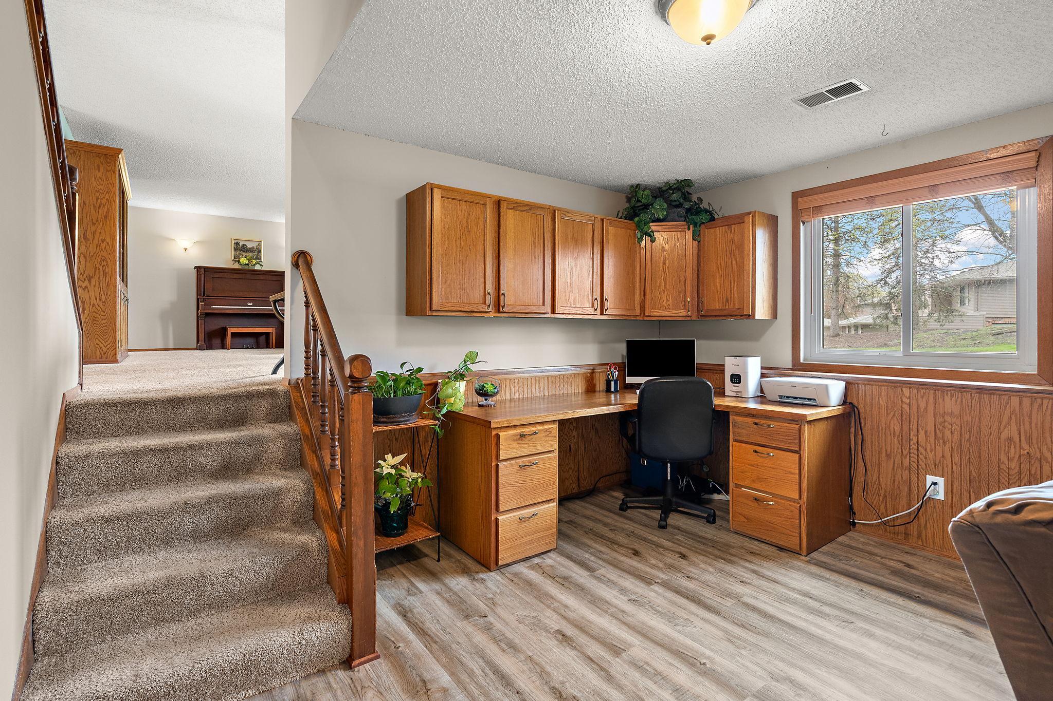 The lower level has a office area with a window view of the front yard and street. The stairs leading to the main level are on the left.