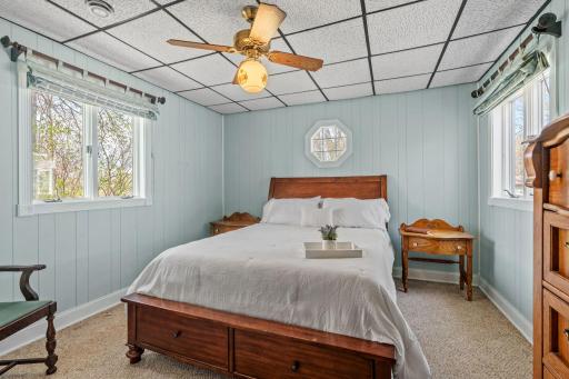 Soft blue walls, warm wood paneling, and a ceiling fan that stirs the evening air, this bedroom feels like every good cabin memory you've ever had, wrapped up in one room.
