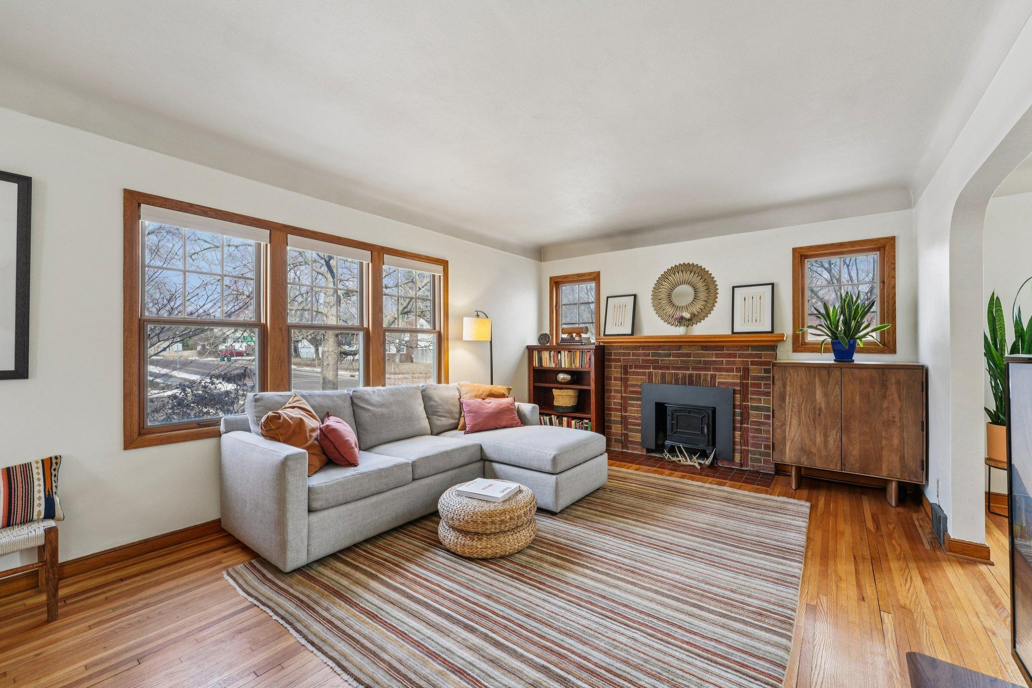Bright living room featuring beautiful original woodwork, hardwood floors, and a cozy fireplace with classic brick surround.