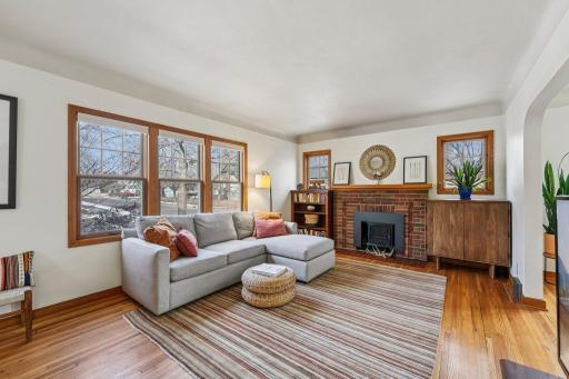 Bright living room featuring beautiful original woodwork, hardwood floors, and a cozy fireplace with classic brick surround.