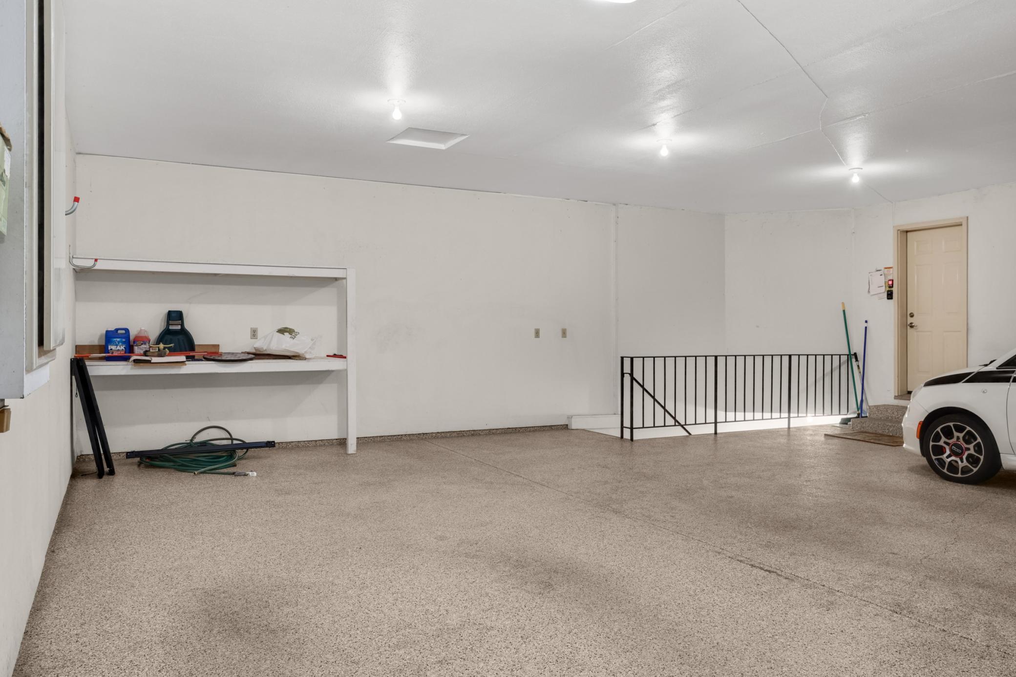 Very large garage with storage shelving and stairs that lead down to a 2nd entrance into the home.