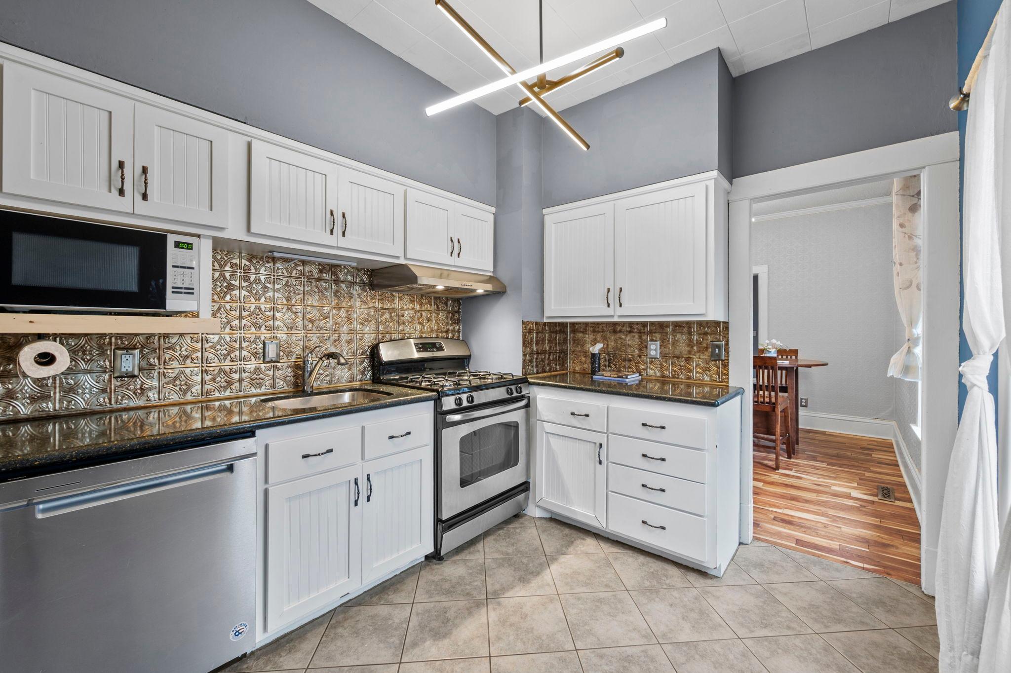 The kitchen offers a cozy yet functional layout, complete with stainless steel appliances, including a gas stove, a stylish backsplash, and a statement light fixture that adds a touch of character.