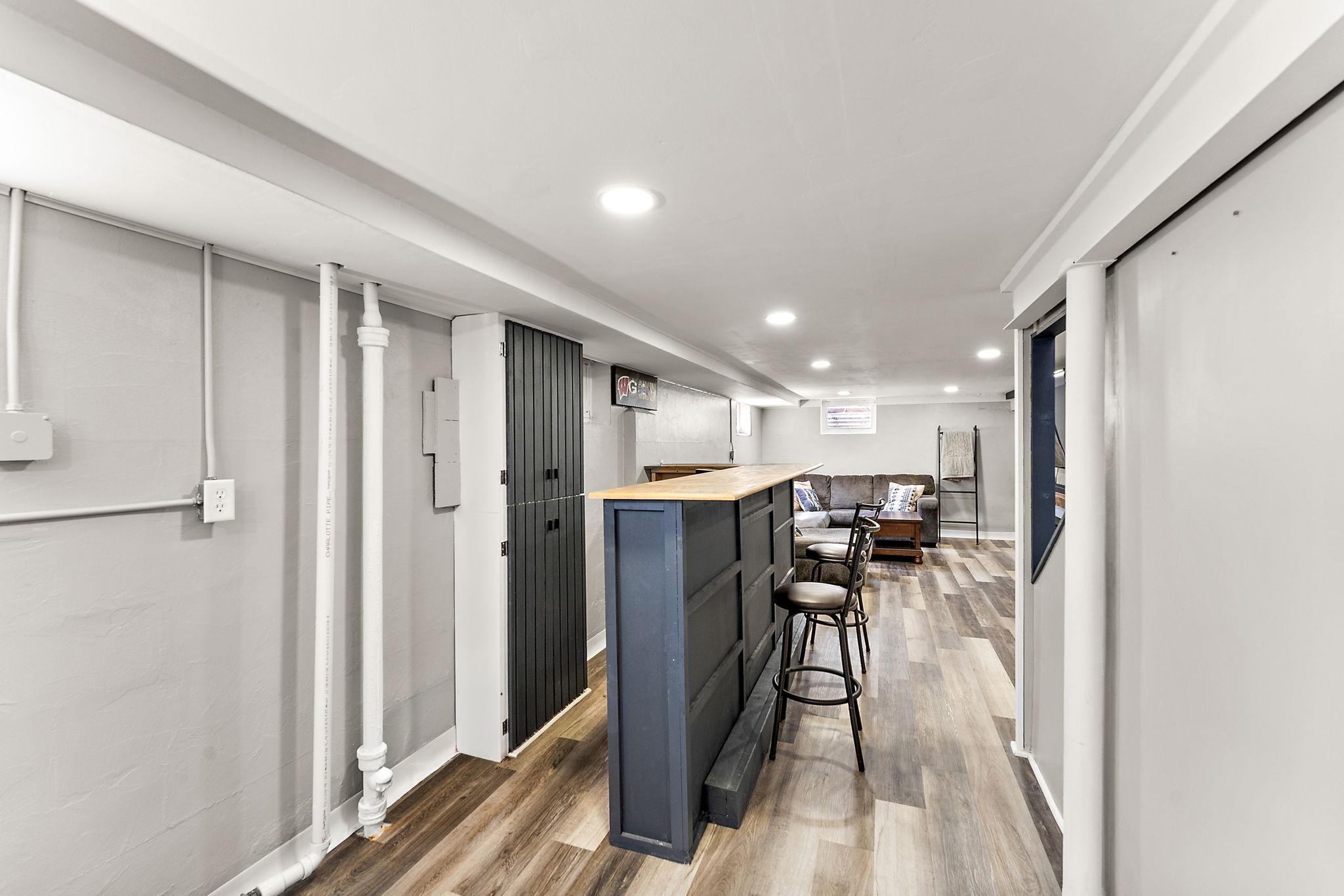 A view from the lower level flex space showing the bar and the recreation area beyond. The lower level is fully finished with new paint, flooring, recessed lighting and drywall, increasing the home's livable space.