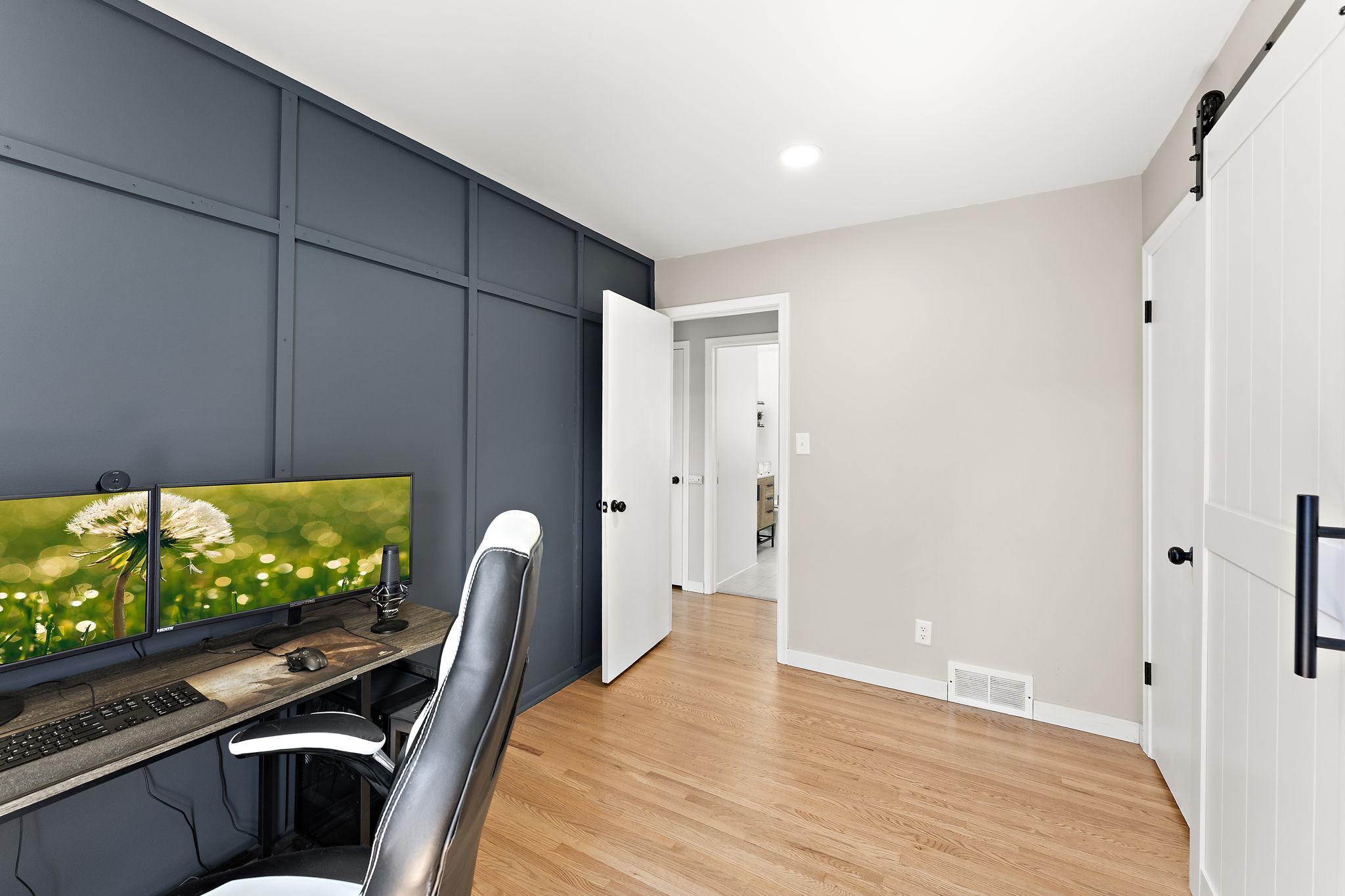 The main floor office space is accessible from the kitchen on the right through the closed barn door and also from the hallway visible through the open door beyond which also is a glimpse of the main floor bathroom.