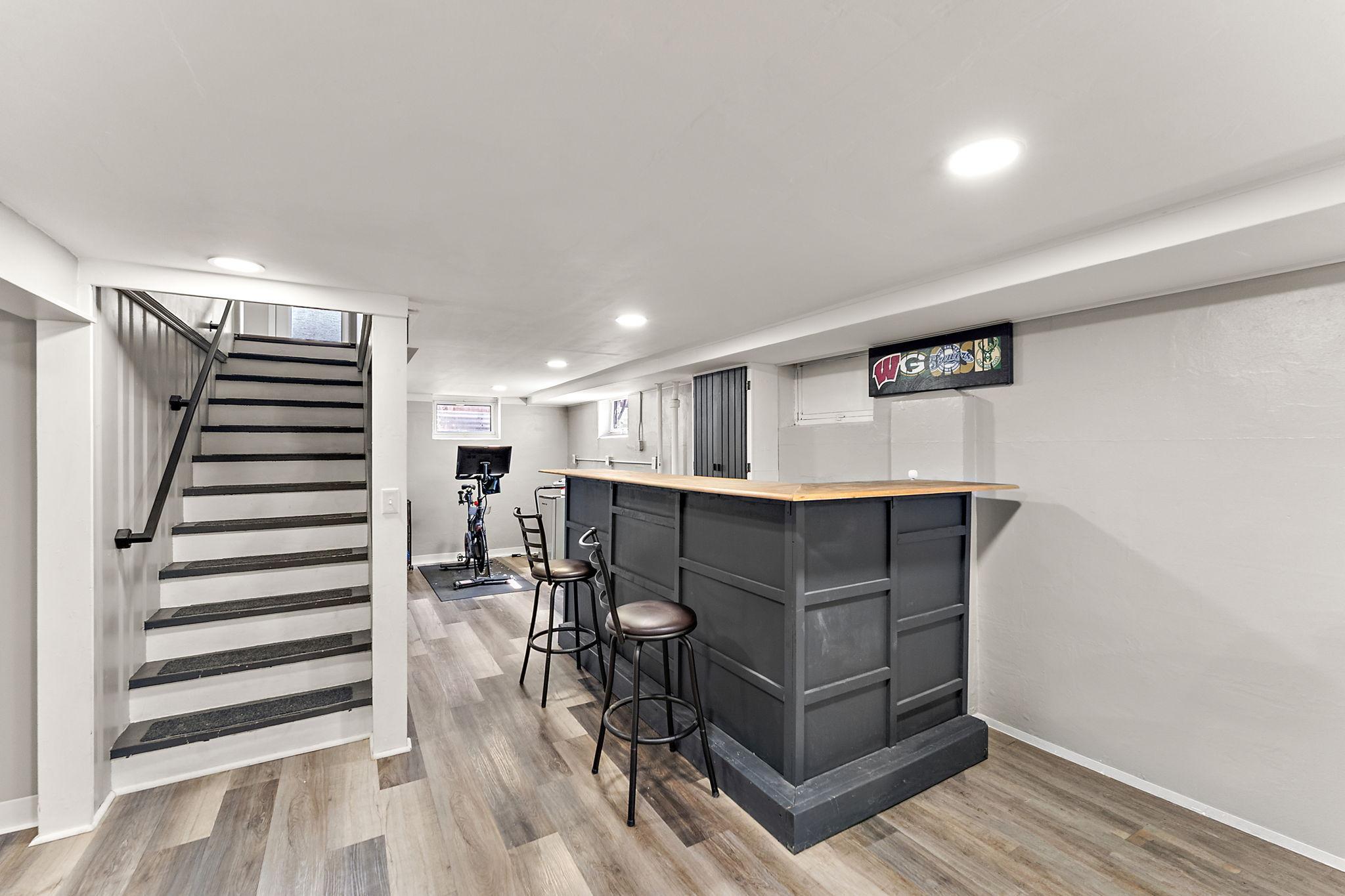 The new bar is on the right with a flex space beyond and a hallway to the left of the stairs, leading to the lower level bedroom and bathroom.
