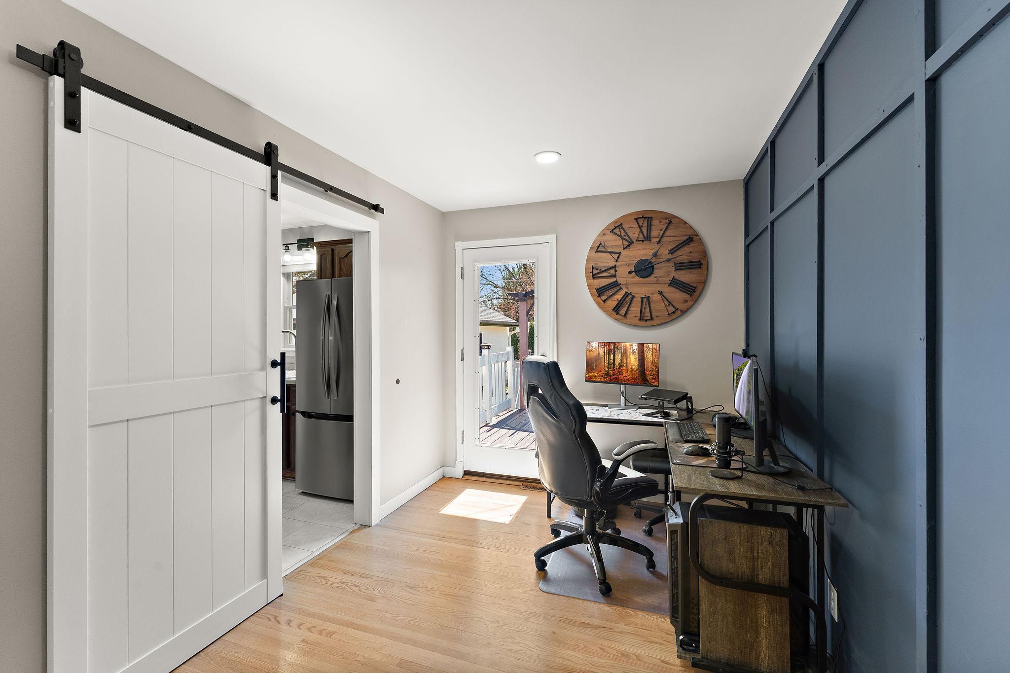 The main floor has an office space and/or additional bedroom with a barn door to close off the kitchen with access to the deck visible across the room.