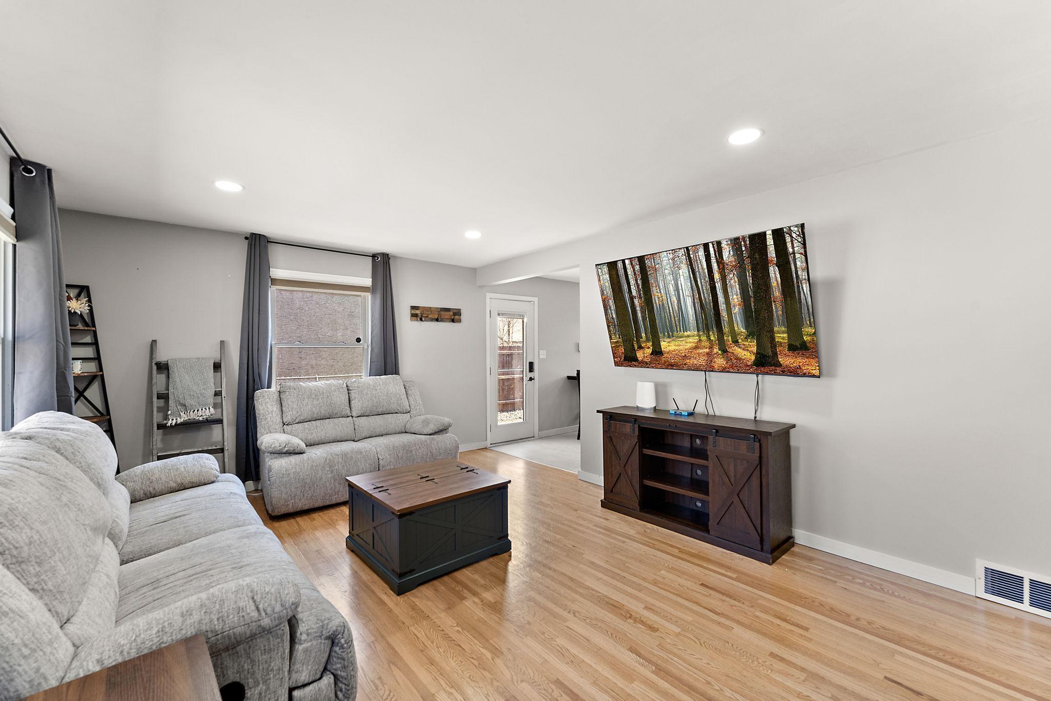 Standing near the front door leading in from the street and looking into the living room with the side door to the front of the garage visible across the room.