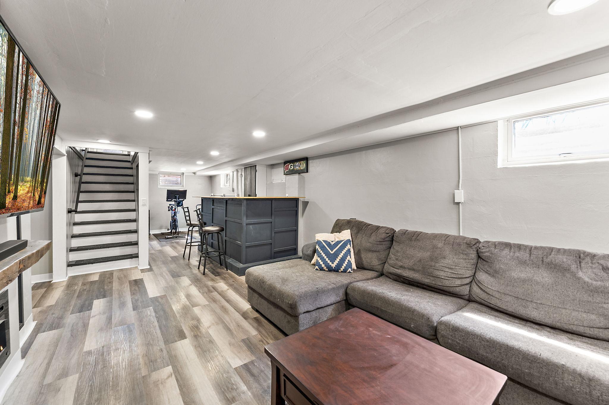 The lower level features new flooring, an electric fireplace on the far left and a newly installed bar with recessed lighting. A perfect place to host or unwind after a long day.