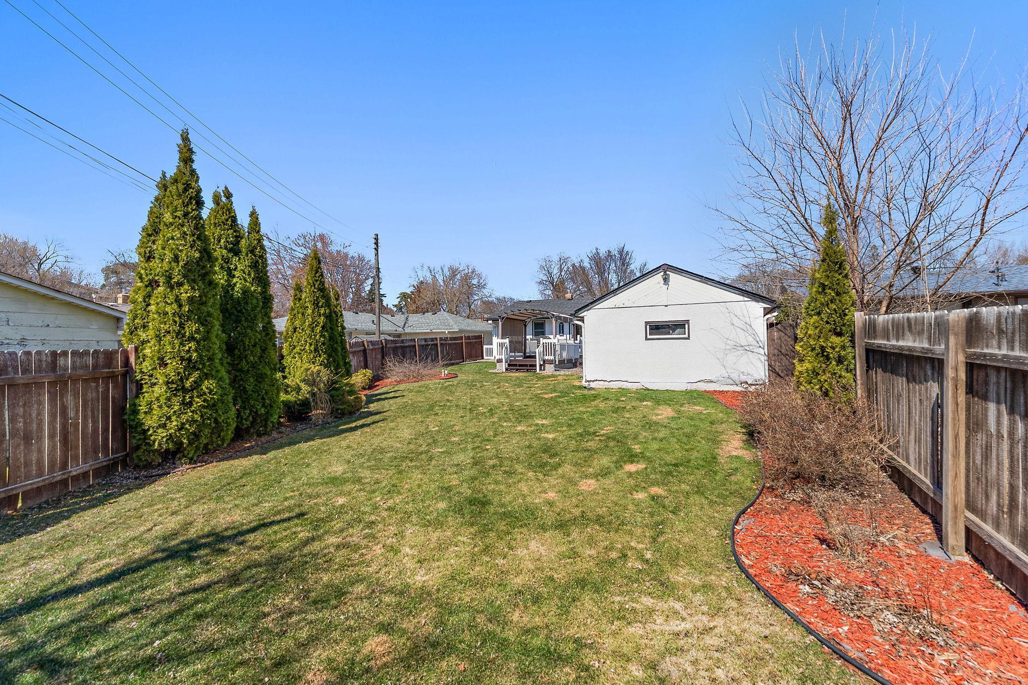 A view from the far back of the yard showing the back of the garage and house. There is plenty of yard space for outdoor hobbies and games.
