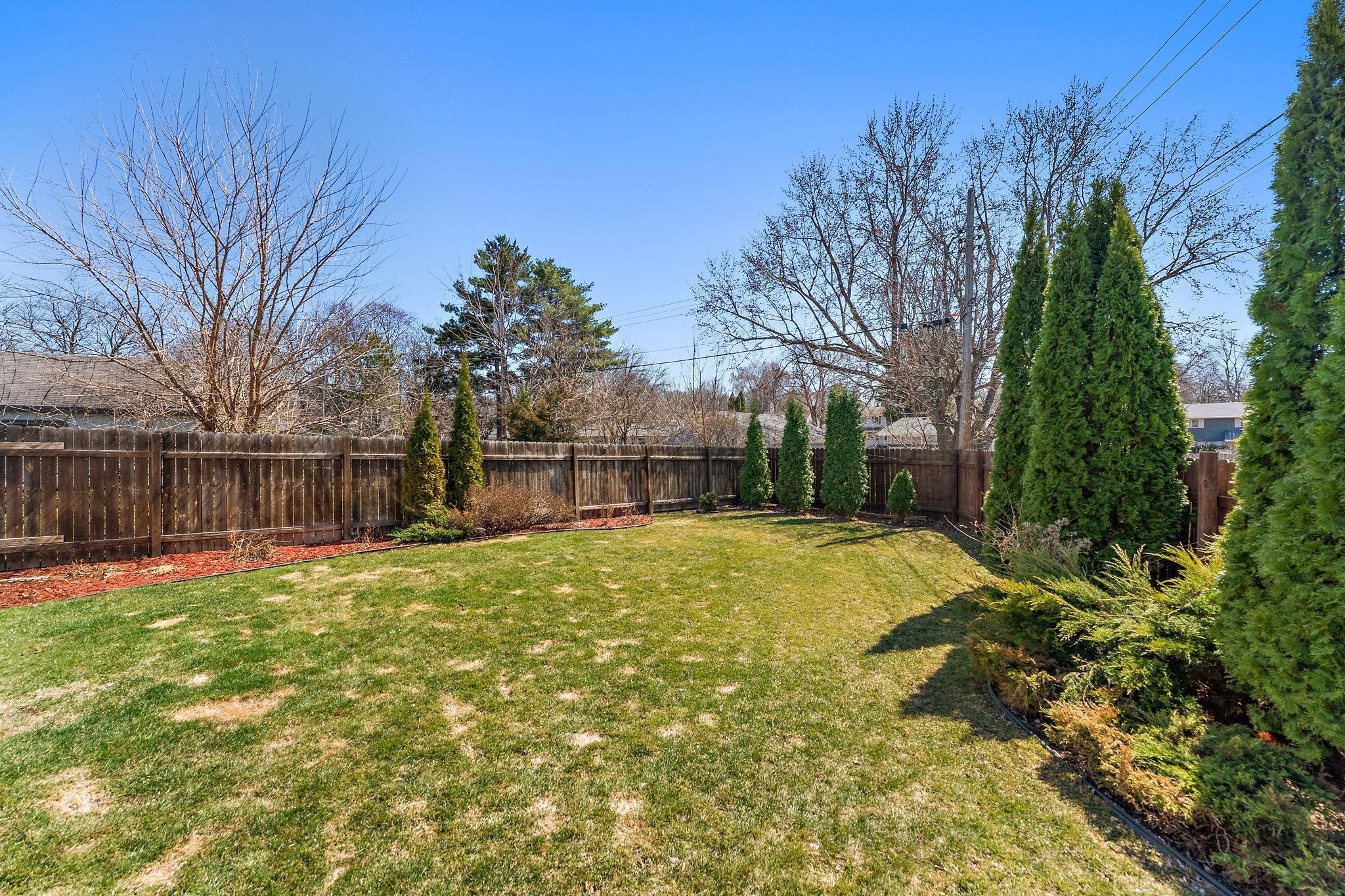 The backyard has mature arbor vitae trees and flower bed space along the fence, perfect for creating a lovely garden retreat.