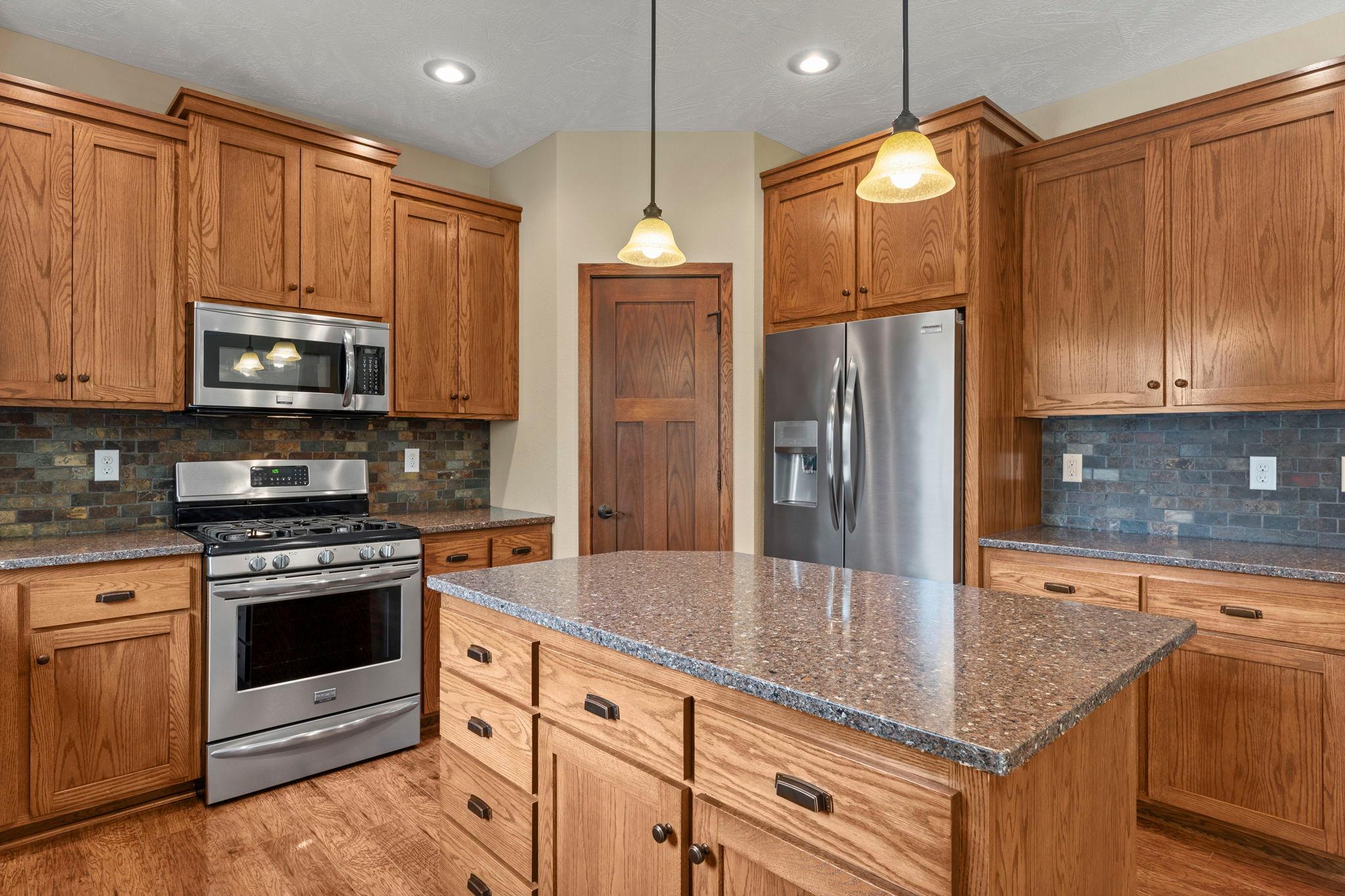 Gorgeous kitchen accented by oak cabinets, stainless appliances, brick backsplash and stone countertops