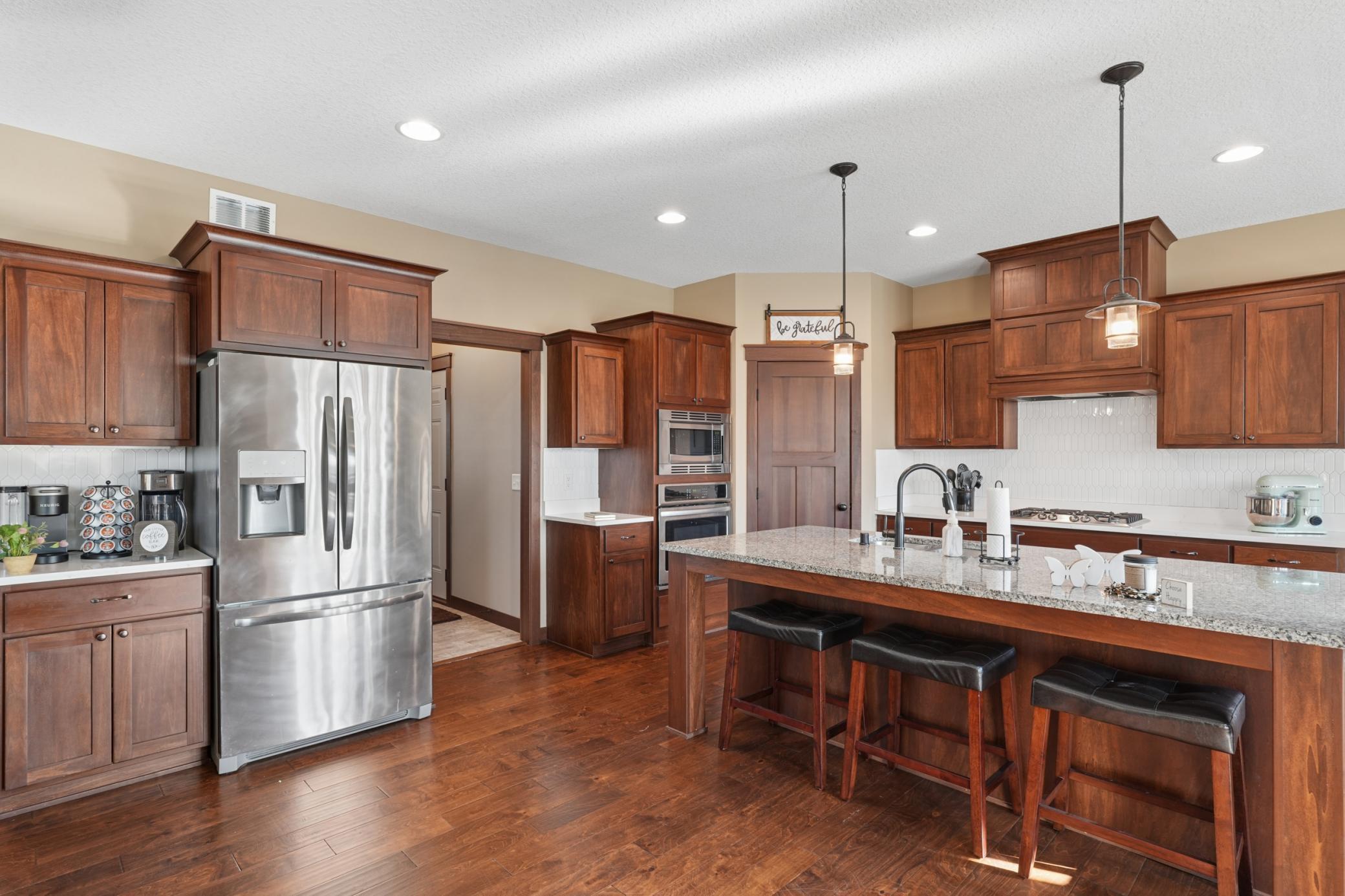 This kitchen boasts premium appliances, walk-in corner pantry, timeless cabinetry, and granite countertops, all bathed in natural light