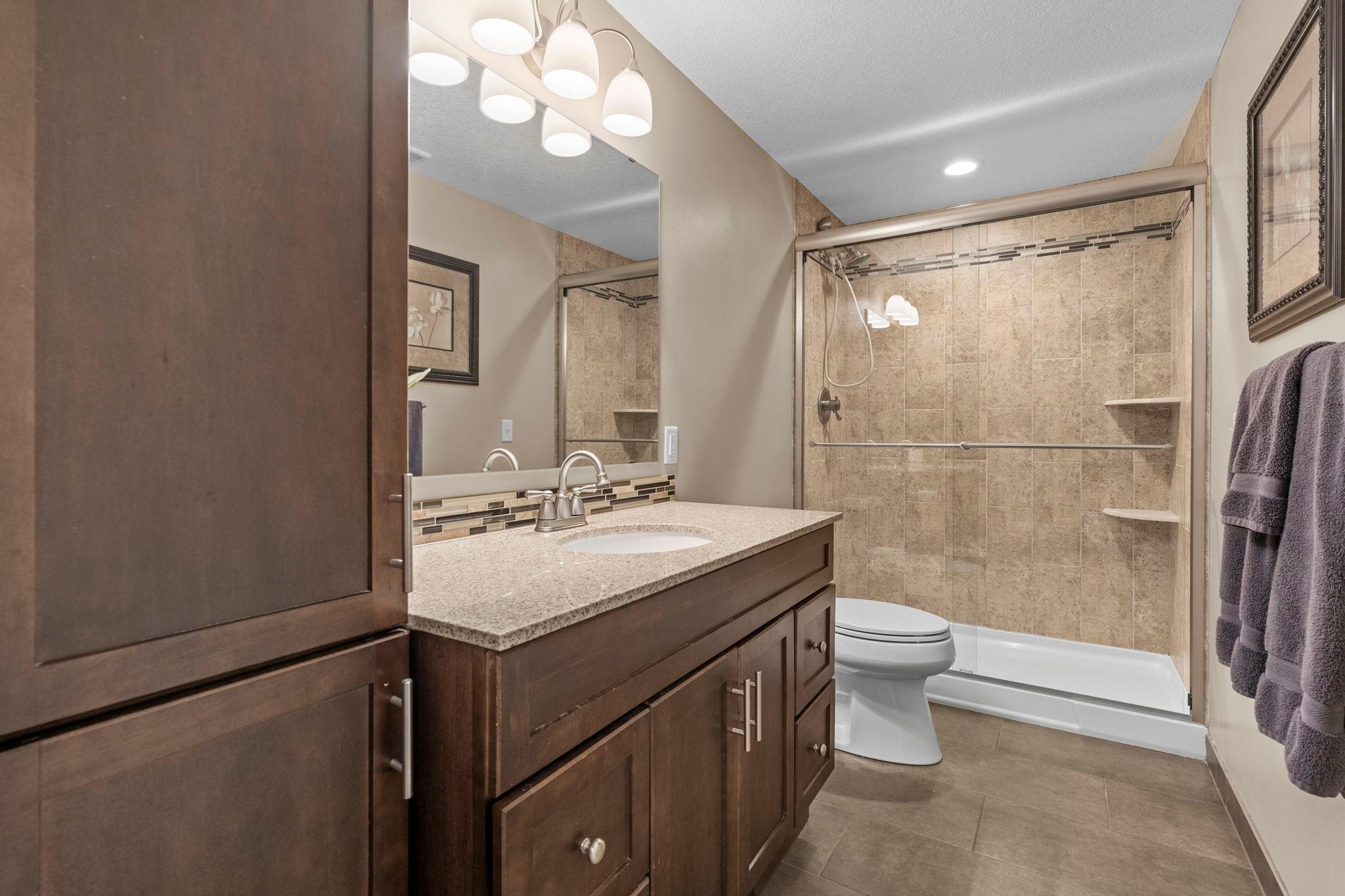 Beautiful 3/4 bathroom with tiled shower, floors, oversized vanity and linen storage.