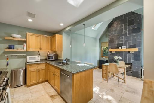 Open-concept kitchen and dining with vaulted ceilings, skylights, granite counters, and a dramatic slate fireplace sourced from the historic Ramsey County Courthouse.