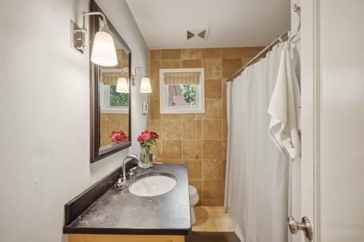 A well-appointed main-floor bath with a stone tile surround, a dark, luxe soapstone vanity, and classic sconce lighting.