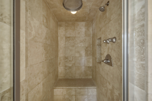 The primary bathroom custom steam shower features floor-to-ceiling luxe tile, a rain showerhead, a built-in niche, and a glass enclosure â a shower worth lingering in.