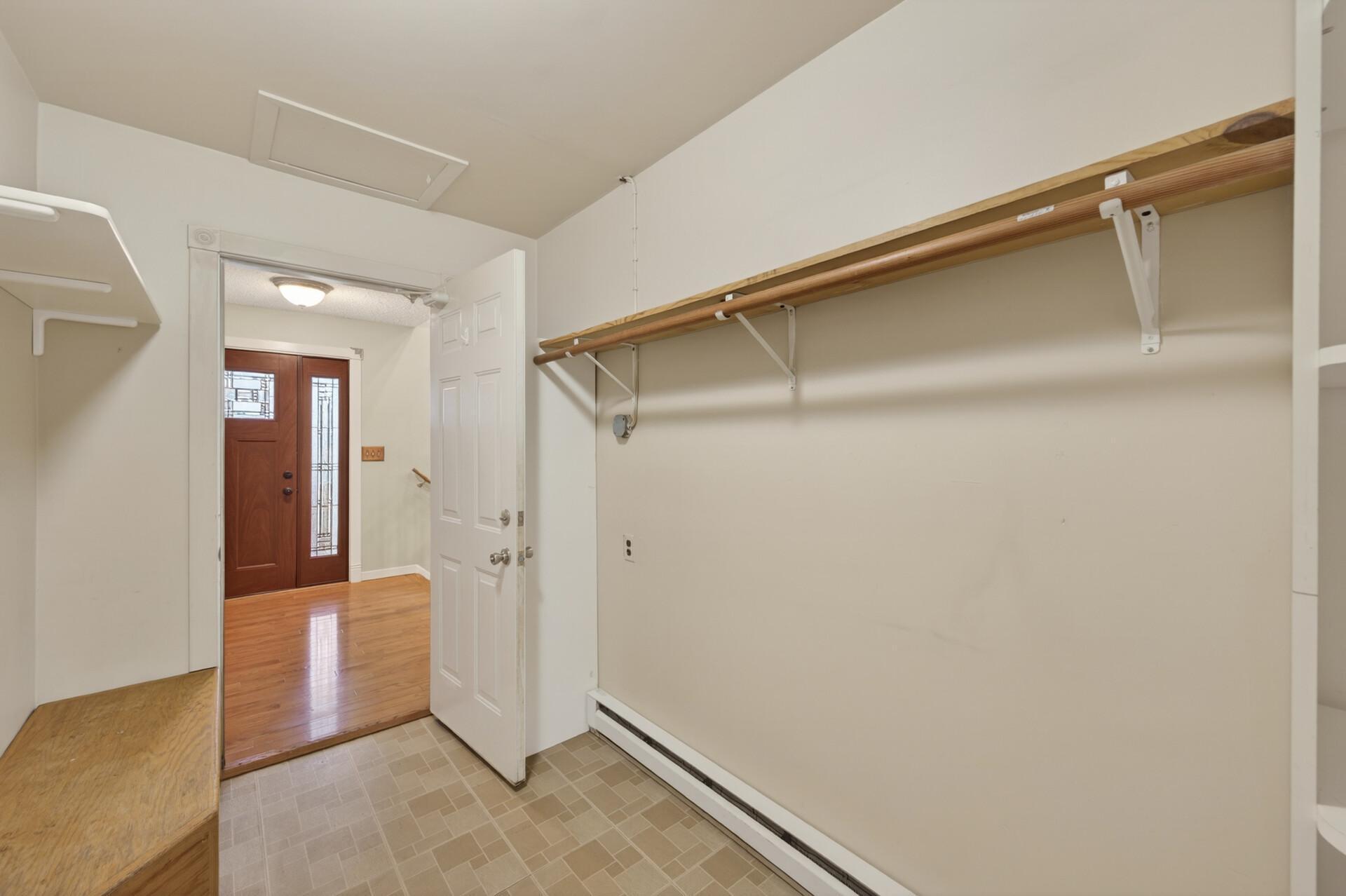 The spacious and functional mudroom features electric heat for year-round comfort, built-in shelving, a convenient bench seat for putting shoes on, and a convenient corner storage cabinet with shelving just out of view.