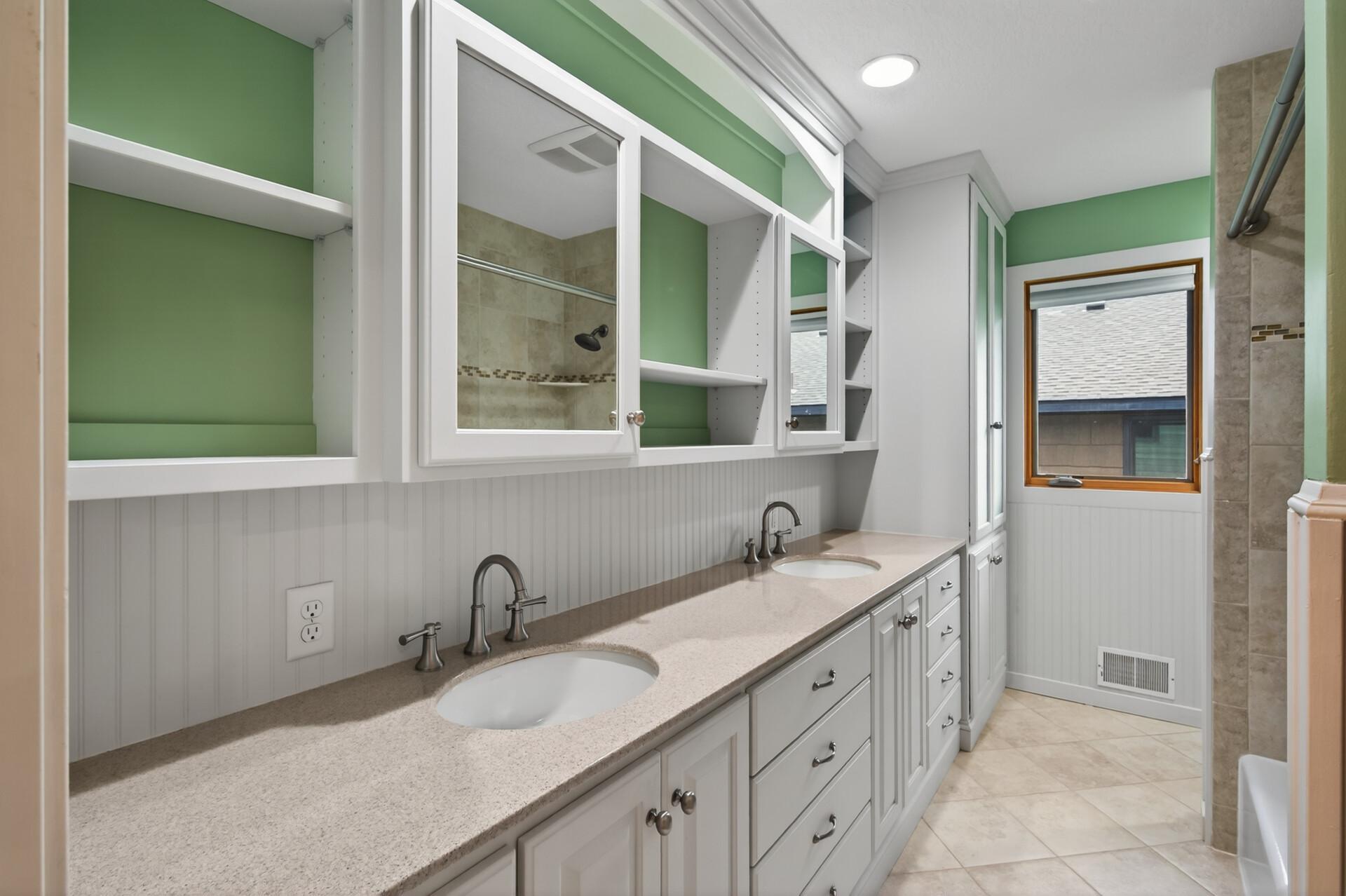 The upper level full bathroom is both stylish and functional, featuring dual sinks, a solid surface countertop, custom cabinetry, including a built-in linen closet, and a convenient pull-out hamper.