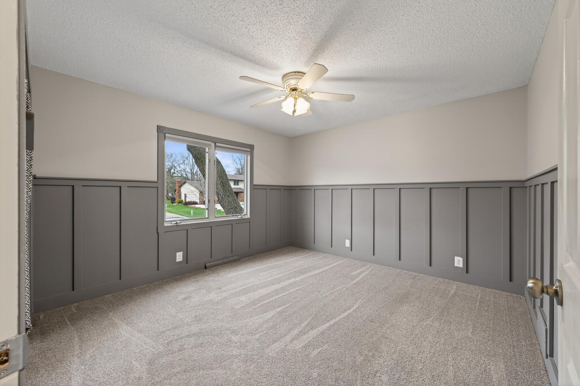 The first bedroom on the upper level offers board and batten wainscotting, adding architectural character and a custom, high-end feel. This room also features plush carpeting, a ceiling fan, and a large closet just out of view.