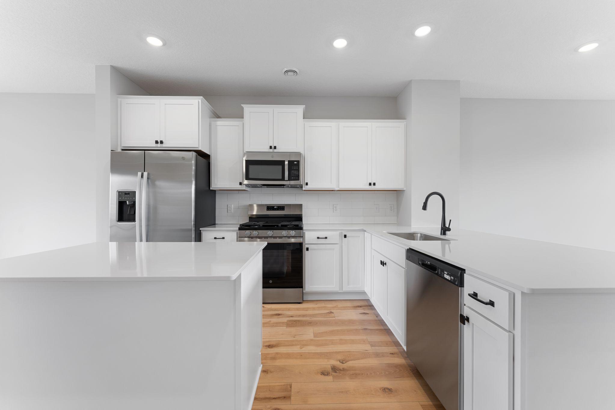 The kitchen is nicely equipped with upgraded cabinets, quartz counters, stainless appliances, and timeless subway tile backsplash. Similar home shown, color & finish can vary.