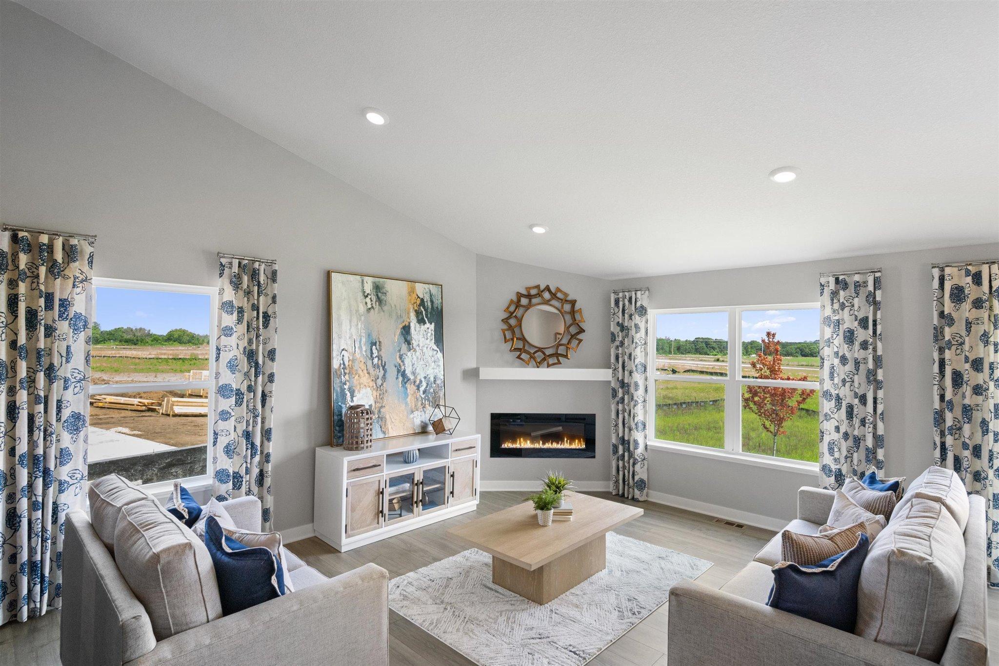 The living room is punctuated by an electric fireplace-which serves as a cozy bookend to the area and highlights a space that's flooded in natural light via soaring windows overlooking the back of the home! Photo is of model home.