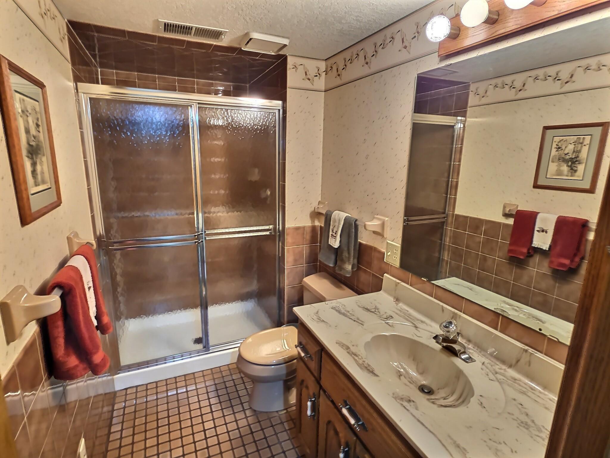 The lower-level bathroom features small tile flooring that adds texture and visual interest while offering durability and easy upkeep. The space includes a clean, modern shower enclosed by a sleek glass door, creating an open, airy feel.
