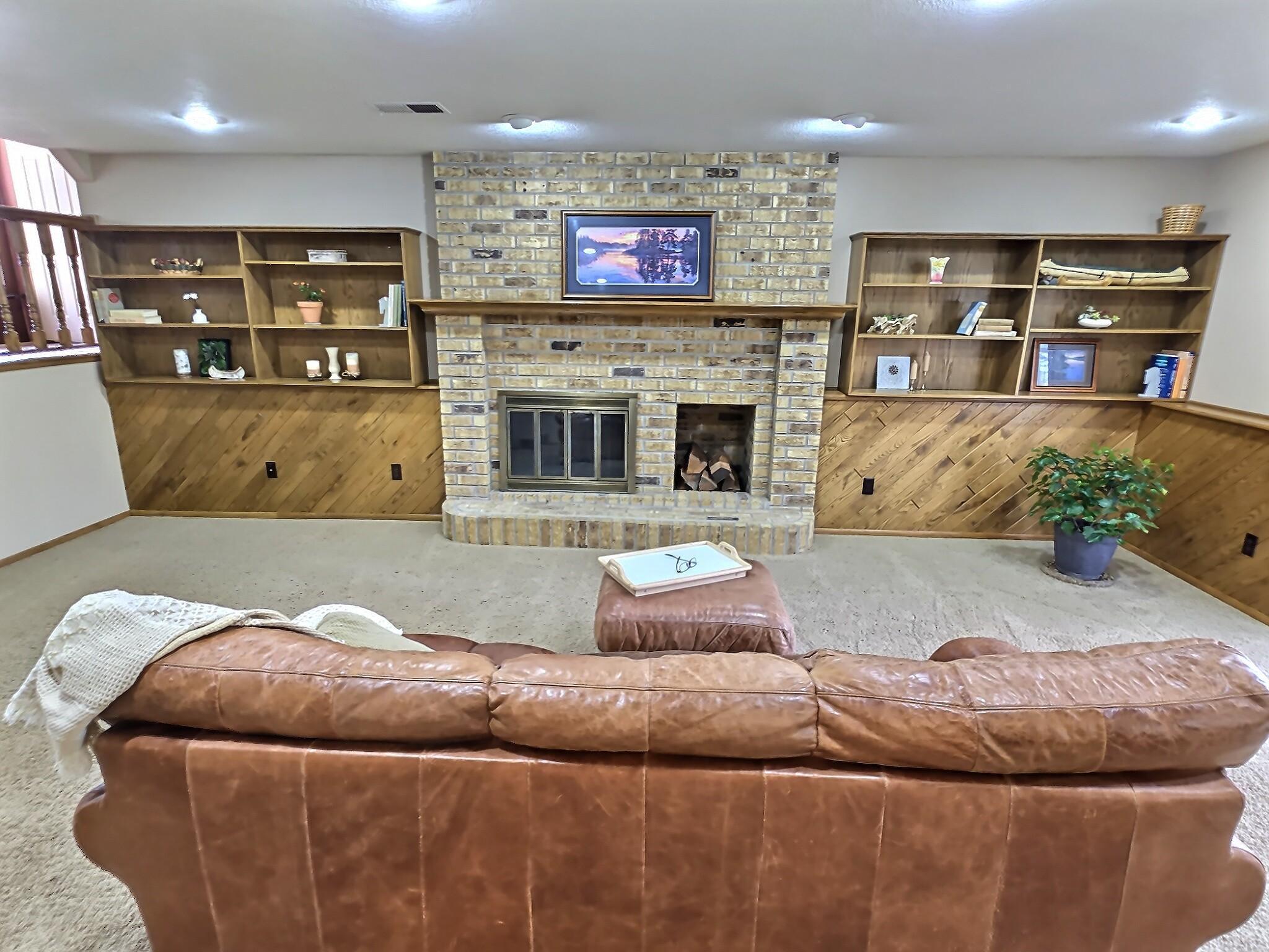 A cozy wood-burning fireplace serves as a warm focal point, framed by neutral brick that adds texture and timeless character. Custom wood shelves provide both function and charm—perfect for displaying books, decor, or personal touches.