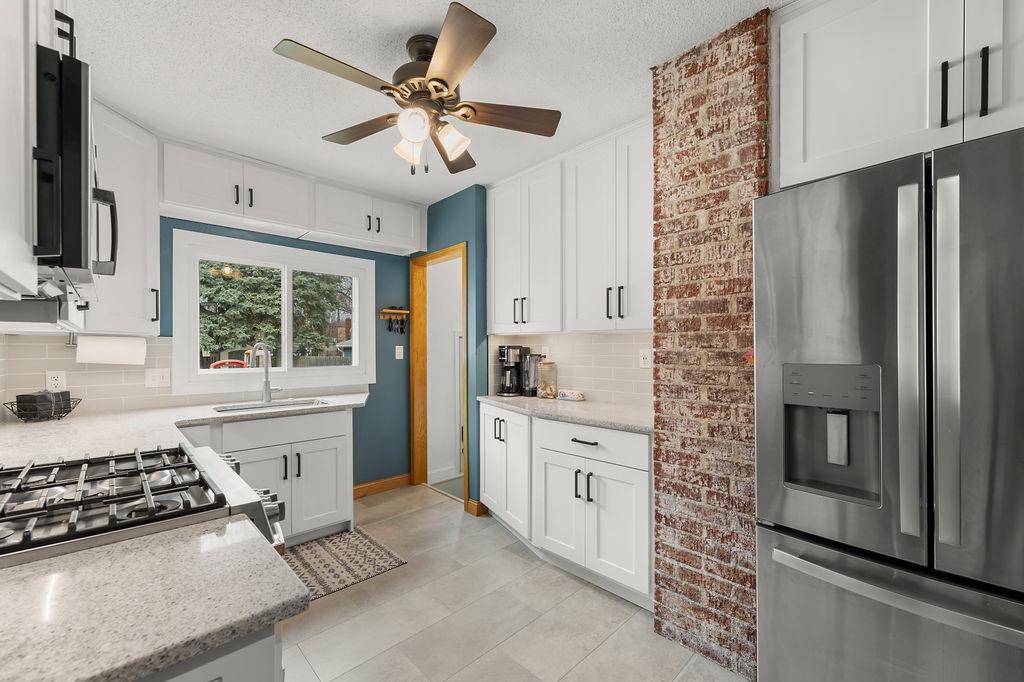 Kitchen features stainless appliances, stone counters, tile backsplash, brick accent