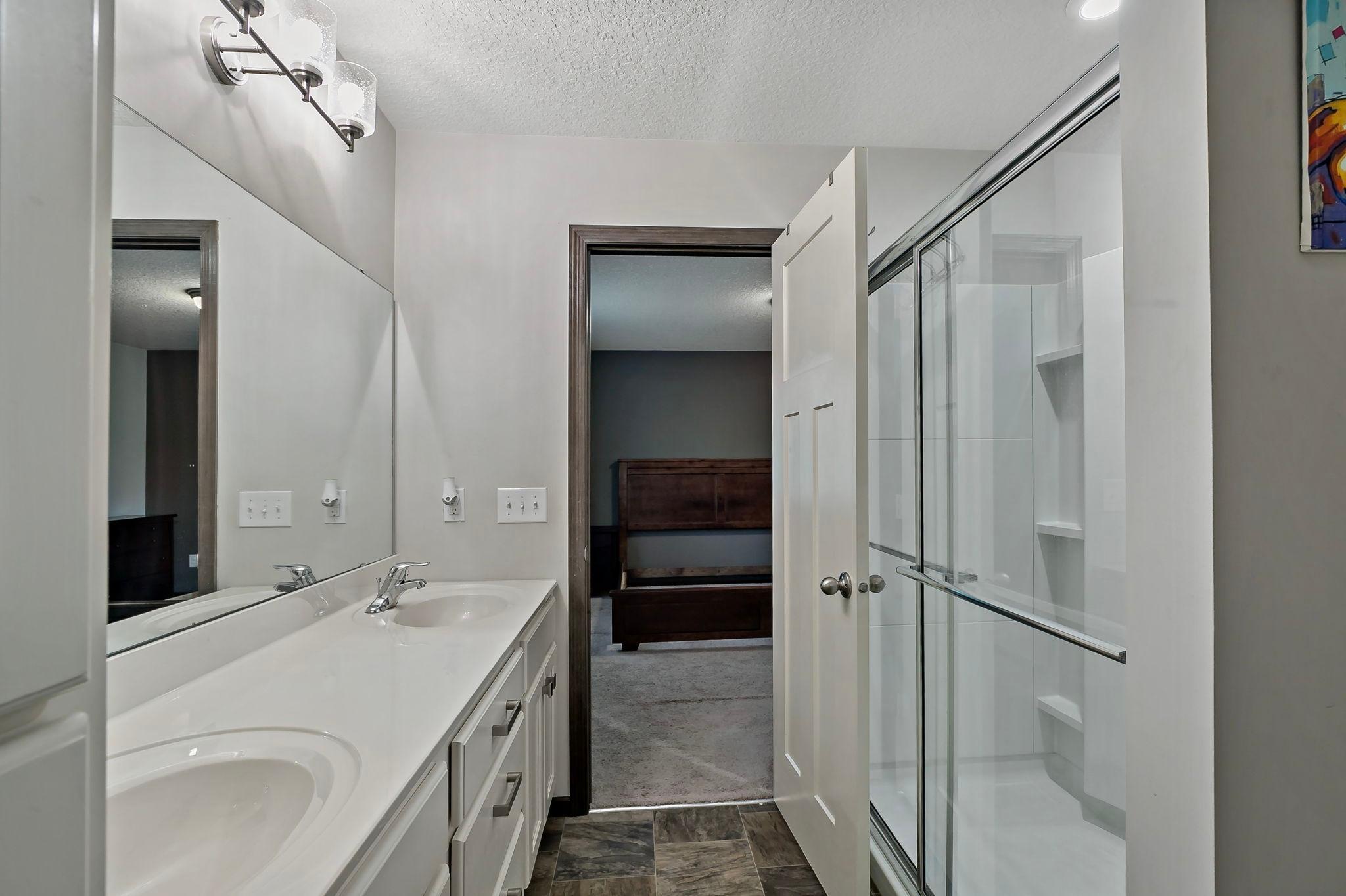 The primary bathroom features dual sinks for added functionality and a spacious step-in shower with a sliding glass door, creating a clean, modern, and comfortable retreat.