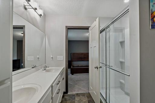 The primary bathroom features dual sinks for added functionality and a spacious step-in shower with a sliding glass door, creating a clean, modern, and comfortable retreat.