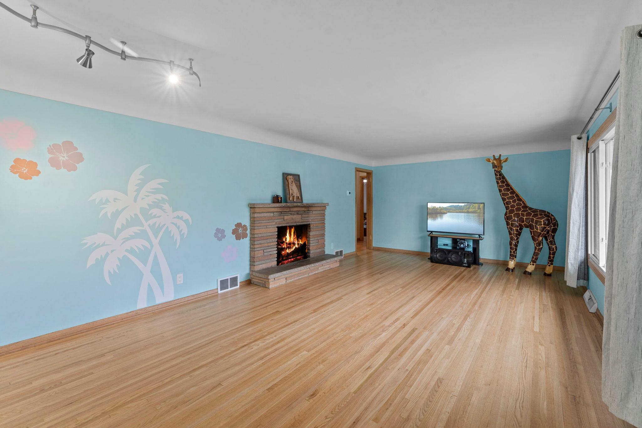 Step inside to a spacious main-level living room featuring gleaming hardwood floors, large windows that fill the space with natural light, and a cozy wood-burning fireplace.