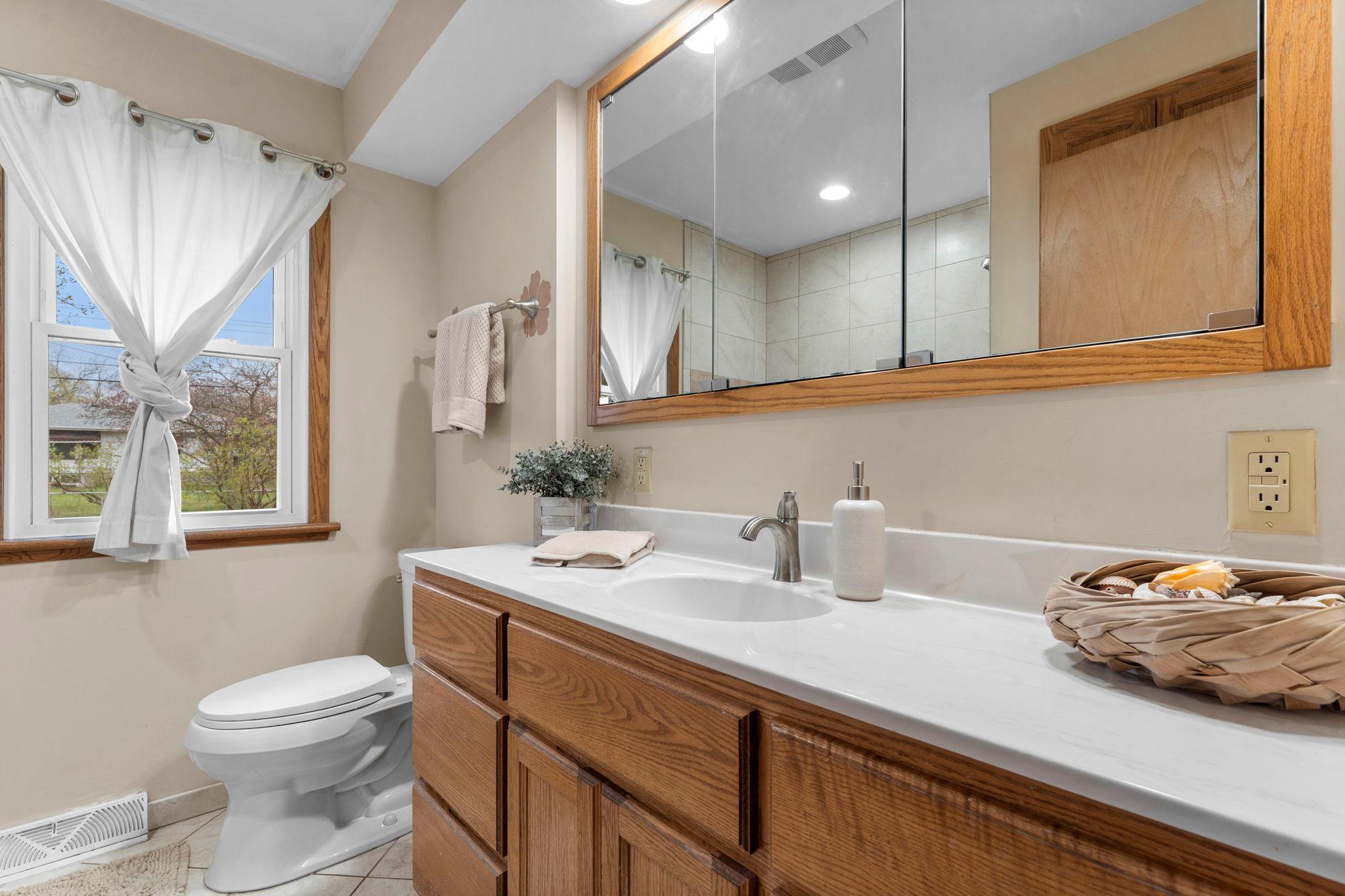 A shared full bathroom is conveniently located nearby, featuring tile flooring, a large single vanity with generous storage, and a tub/shower combination with tiled surround.