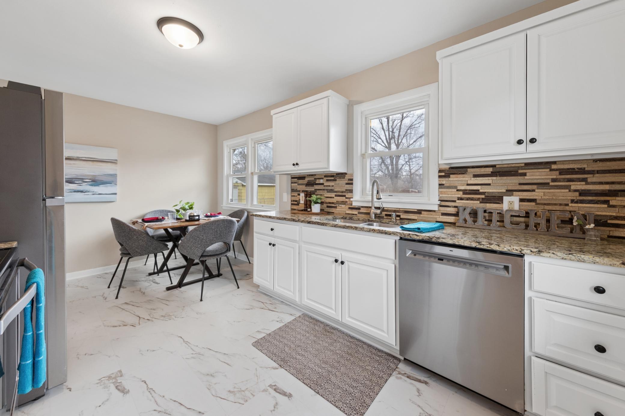 Updated kitchen with white cabinetry, granite countertops, stylish tile backsplash, and stainless steel appliances.