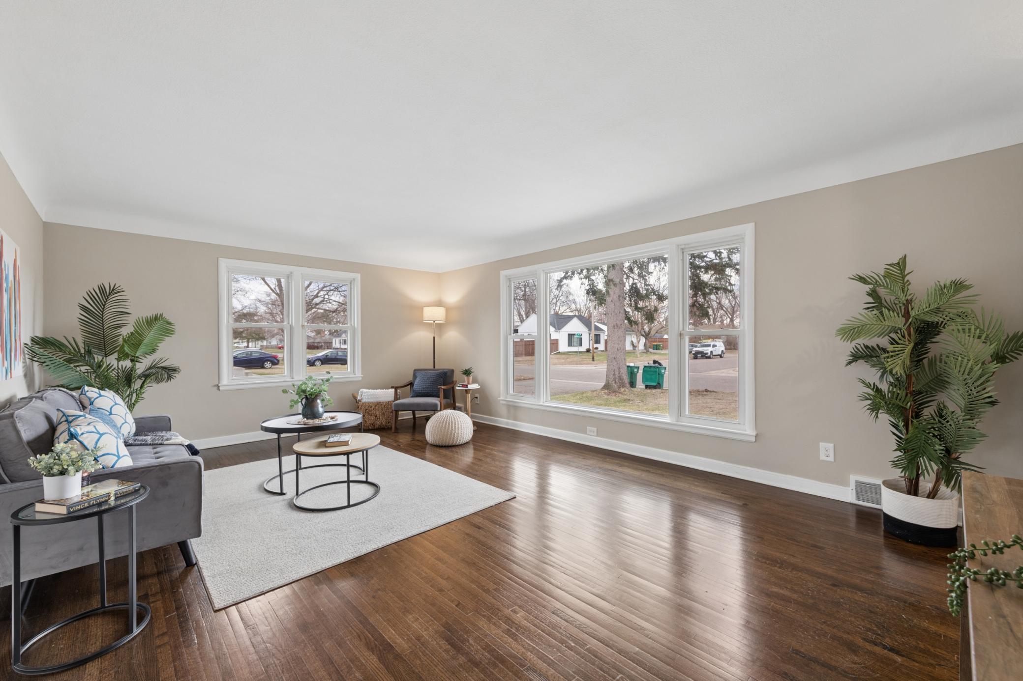Bright and spacious living room filled with natural light, featuring large picture windows and beautifully refinished hardwood floors.